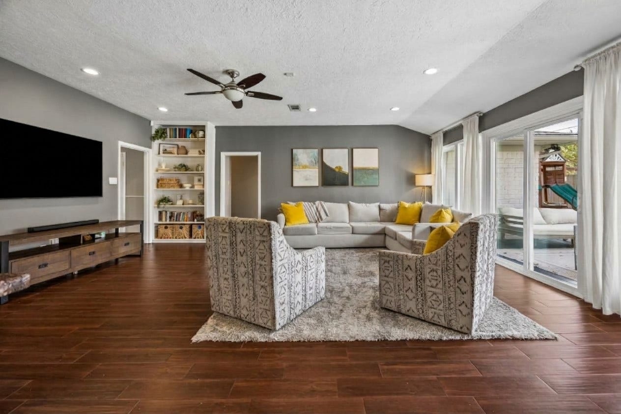 Another view of the family room highlighting the natural light, charming built-ins, and expansive layout that offers incredible flexibility for a variety of furniture arrangements. Note the elegant wood-look tile.