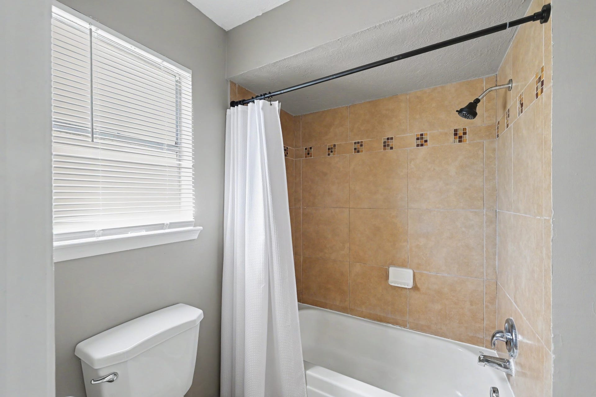 A tiled tub and shower combination with a window that brings in natural light.