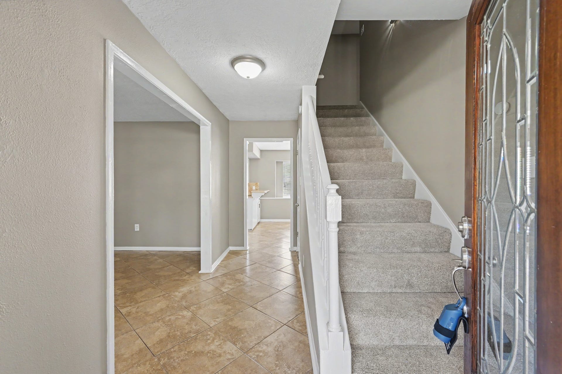 A welcoming entry with neutral tones, tile flooring, and a freshly carpeted staircase.