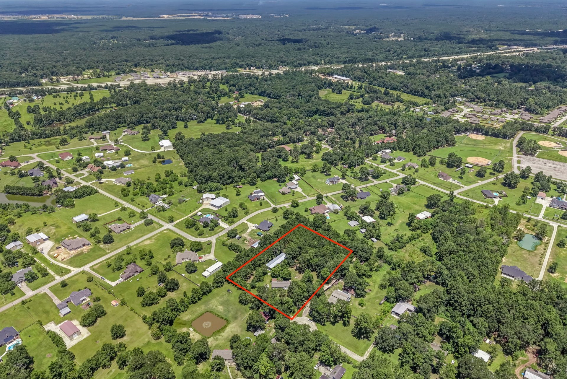 This aerial view showcases the impressive scale of the nearly 3-acre property, where mature trees, open green space, and existing improvements create the perfect balance of privacy, functionality, and endless potential.