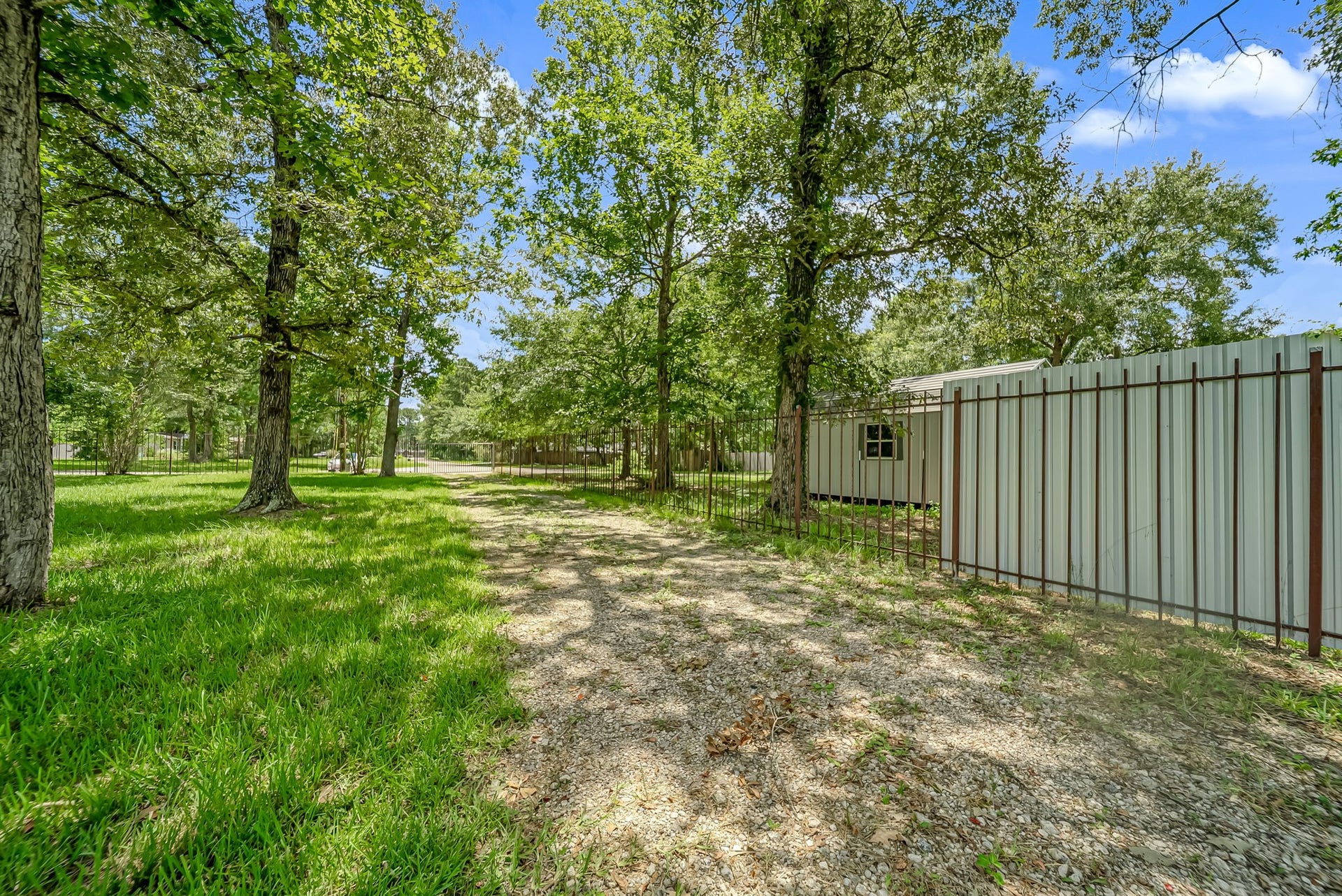 A long gravel driveway leads through mature trees to the gated entrance, offering a private arrival and easy access to the home's fenced living area.