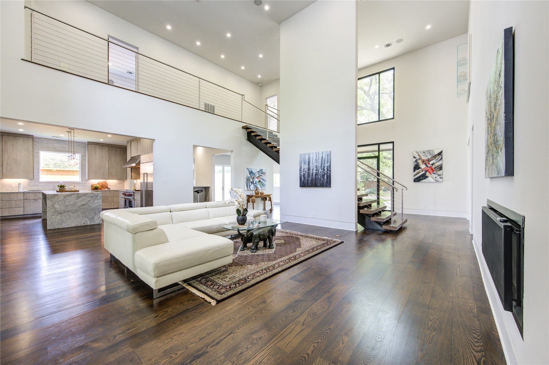 5202 Chesapeake Way, Houston, TX 77056 A spacious open-concept living area with high ceilings and abundant natural light. It includes a sleek kitchen with a large island, contemporary finishes, and a floating staircase leading to an upper level. The stylish design is complemented by dark wood floors, perfect for comfortable living and entertaining.