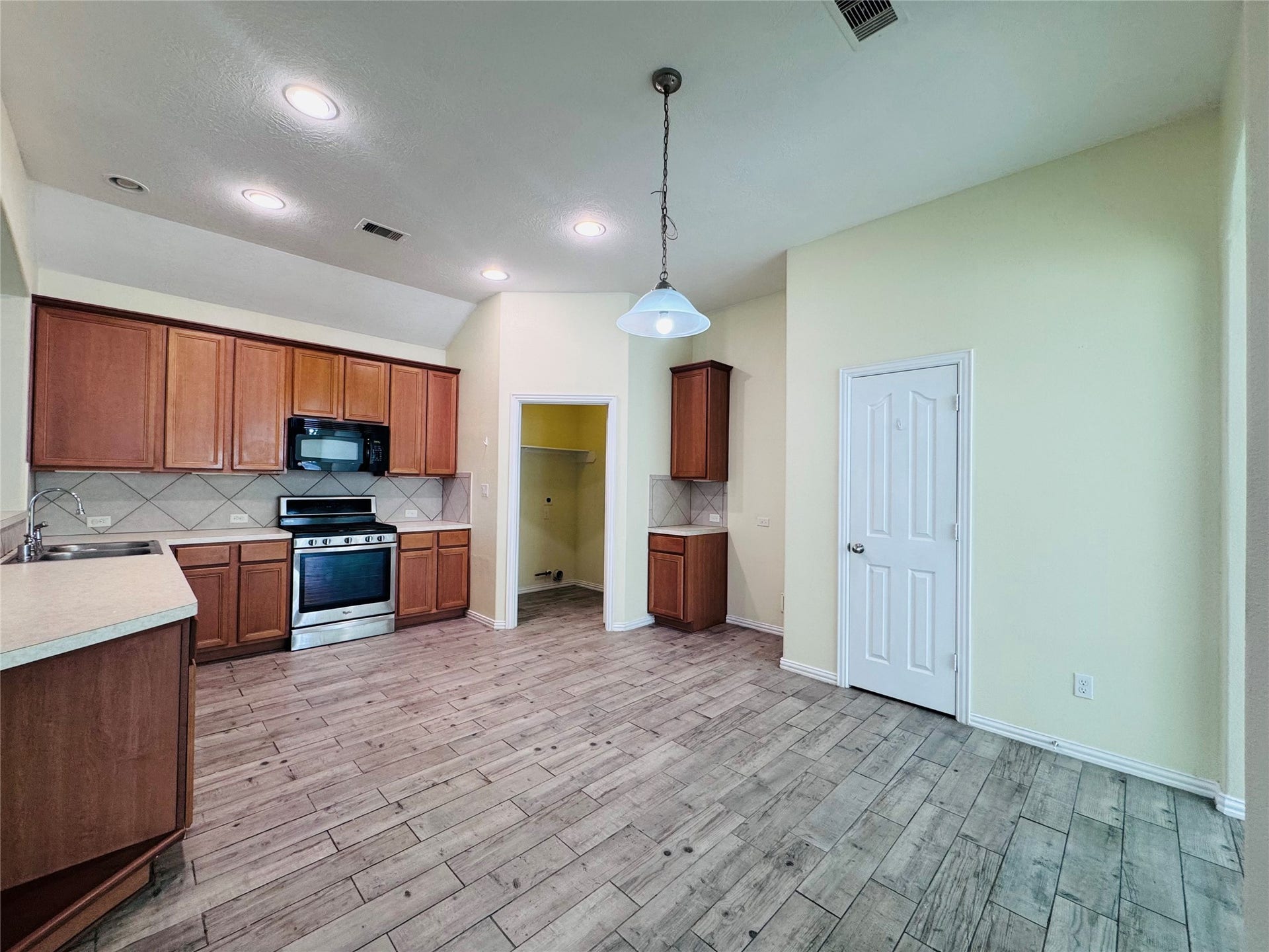 Bright kitchen with modern appliances, warm wood cabinetry, and stylish tile flooring, offering ample space and a cozy dining area.