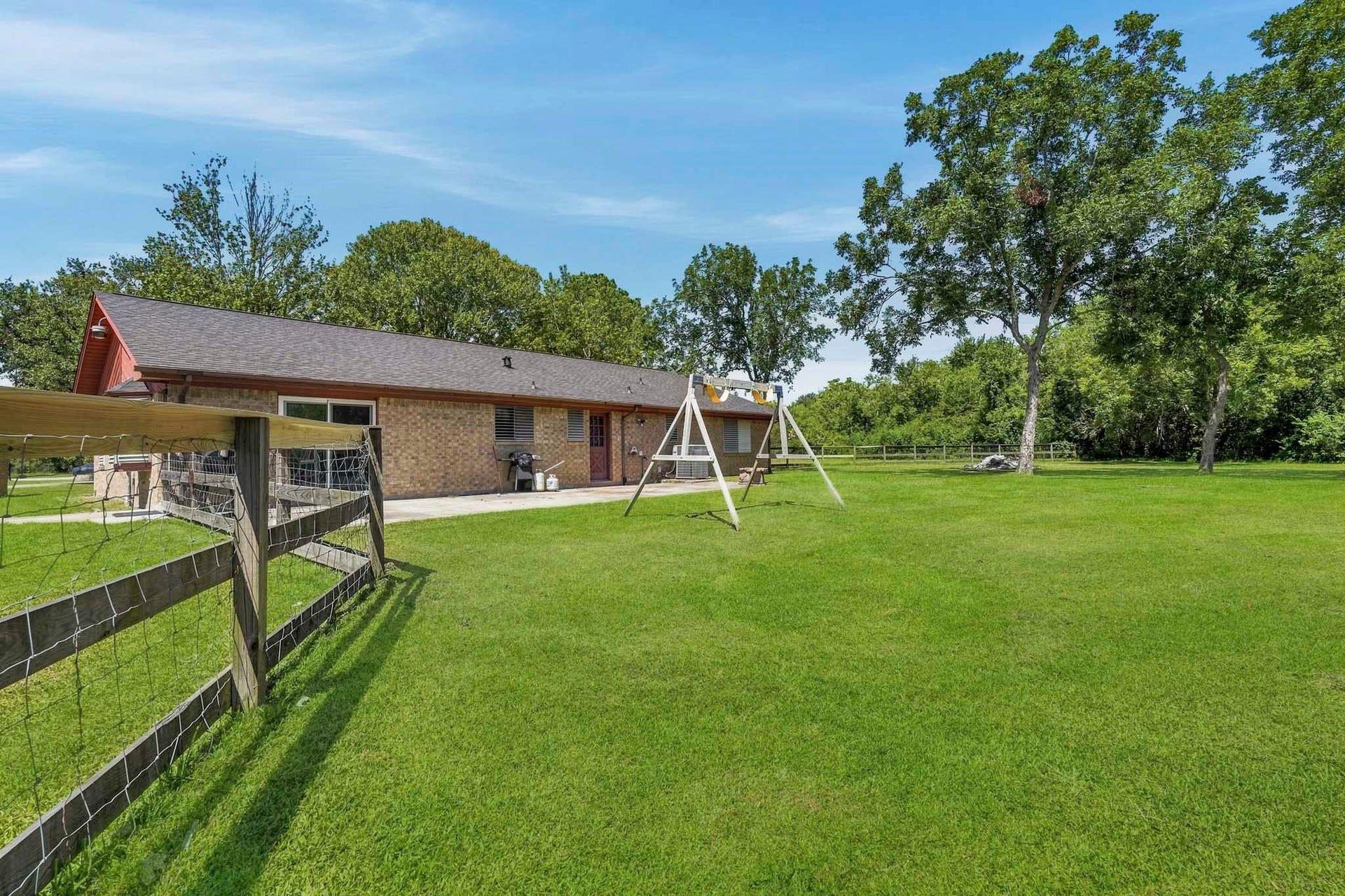 16101 Bluebird Street, Santa Fe, TX 77517 Expansive backyard with lush green lawn, mature trees, and a charming swing set, perfect for outdoor enjoyment and relaxation.