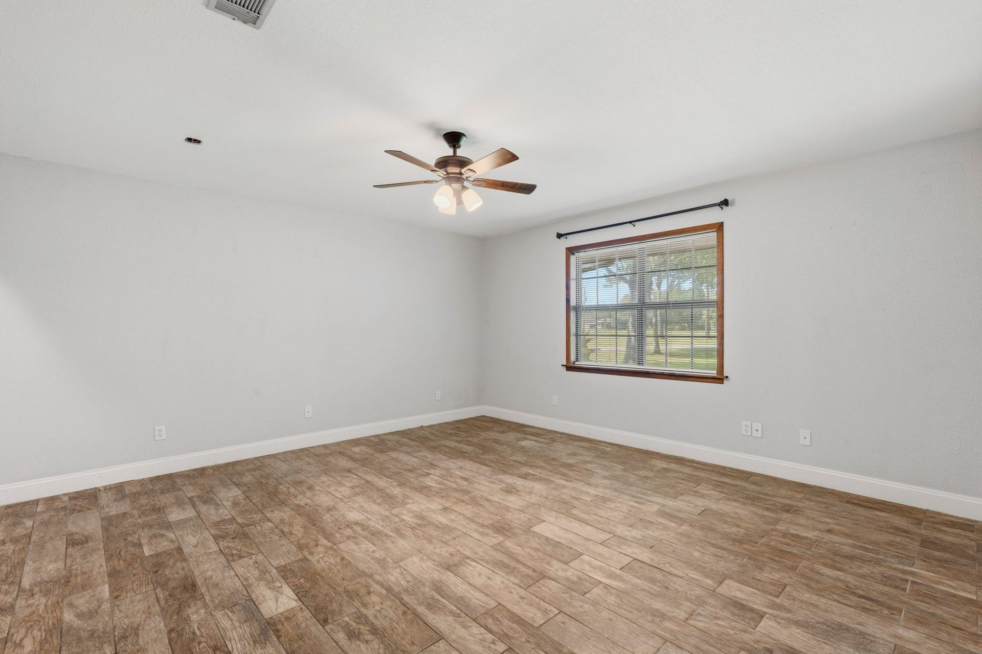 16101 Bluebird Street, Santa Fe, TX 77517 Spacious third bedroom with elegant wood-look flooring, a ceiling fan, and a large window offering serene views.