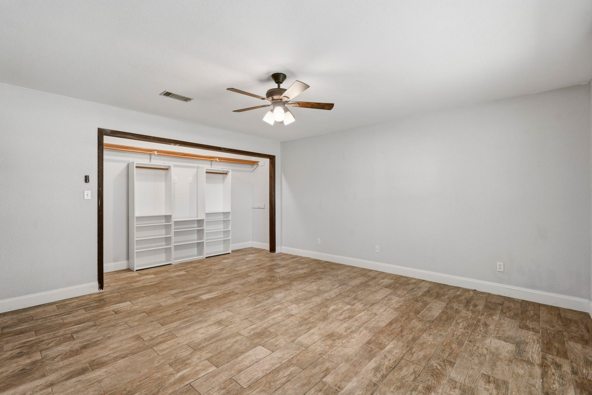 16101 Bluebird Street, Santa Fe, TX 77517 Spacious third bedroom with elegant wood-look tile flooring, featuring a ceiling fan and a large open closet with ample shelving for organized storage.