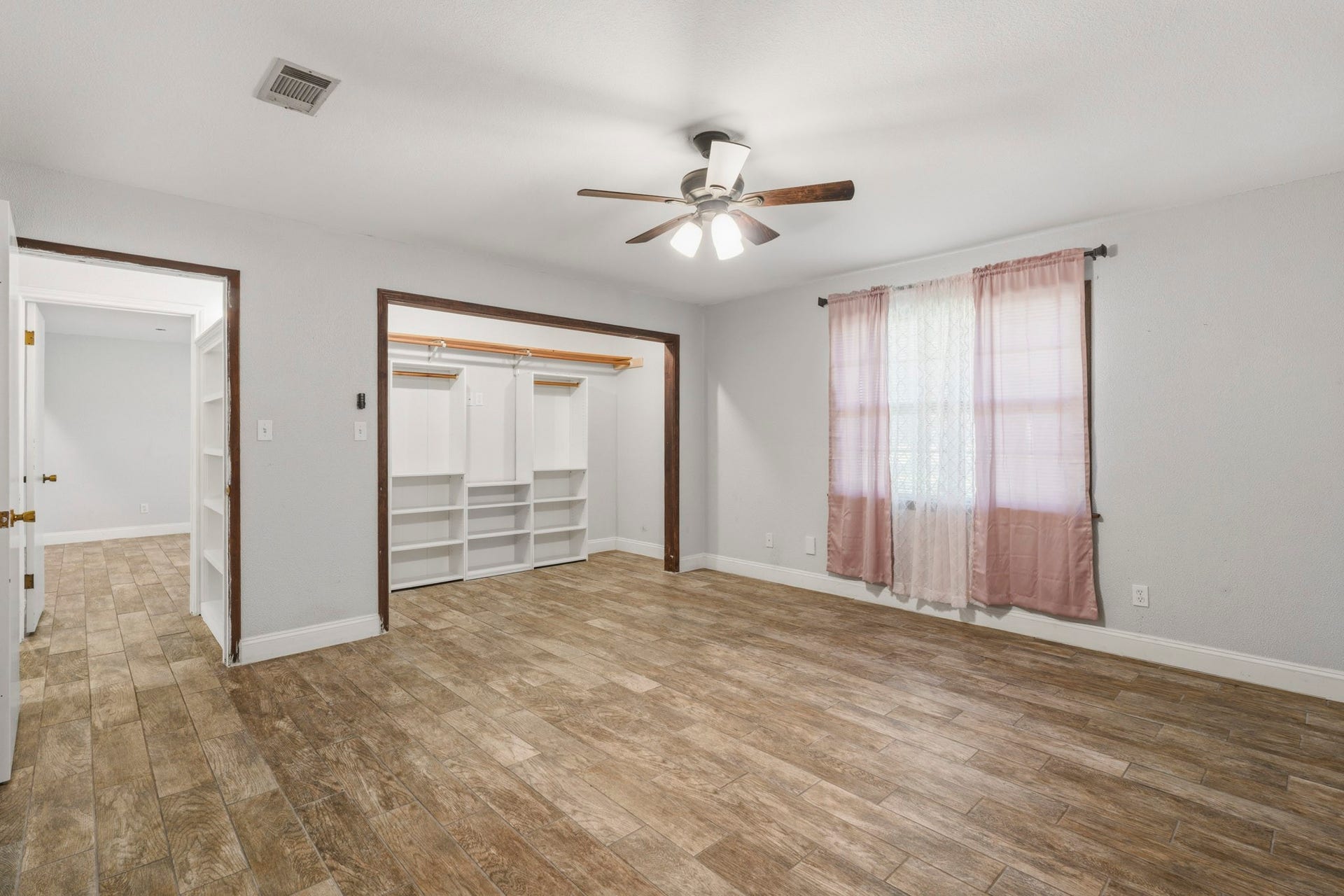 16101 Bluebird Street, Santa Fe, TX 77517 Spacious secondary bedroom featuring wood-look tile flooring, ample closet space with built-in shelving, and a ceiling fan for comfort. Natural light streams through the window, enhancing the room's warmth.