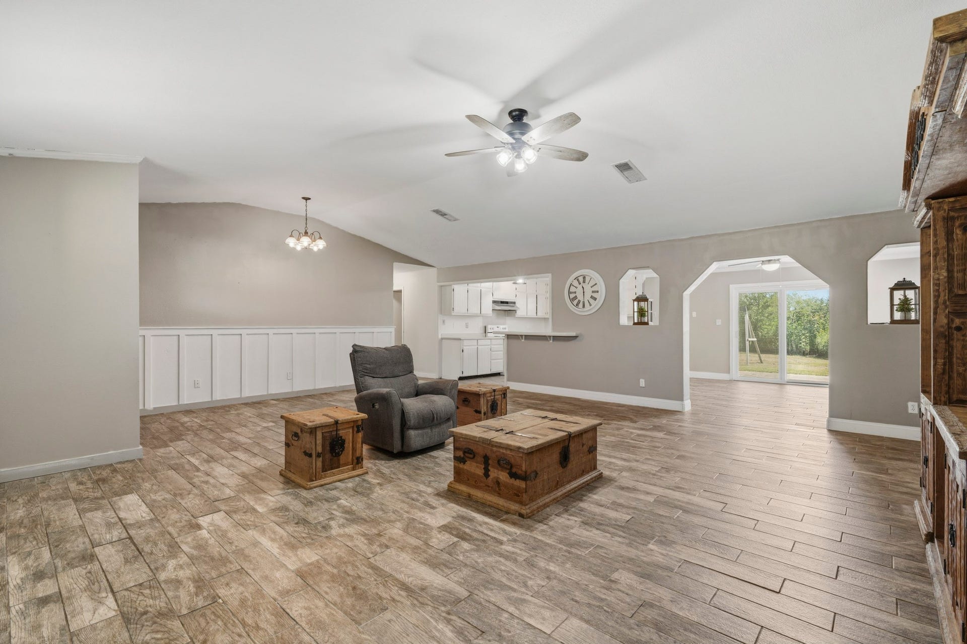 16101 Bluebird Street, Santa Fe, TX 77517 Spacious open-concept living area with wood-look tile flooring. The adjoining kitchen offers white cabinetry and modern lighting, leading to a bright dining area with sliding glass doors that open to a lush backyard view.
