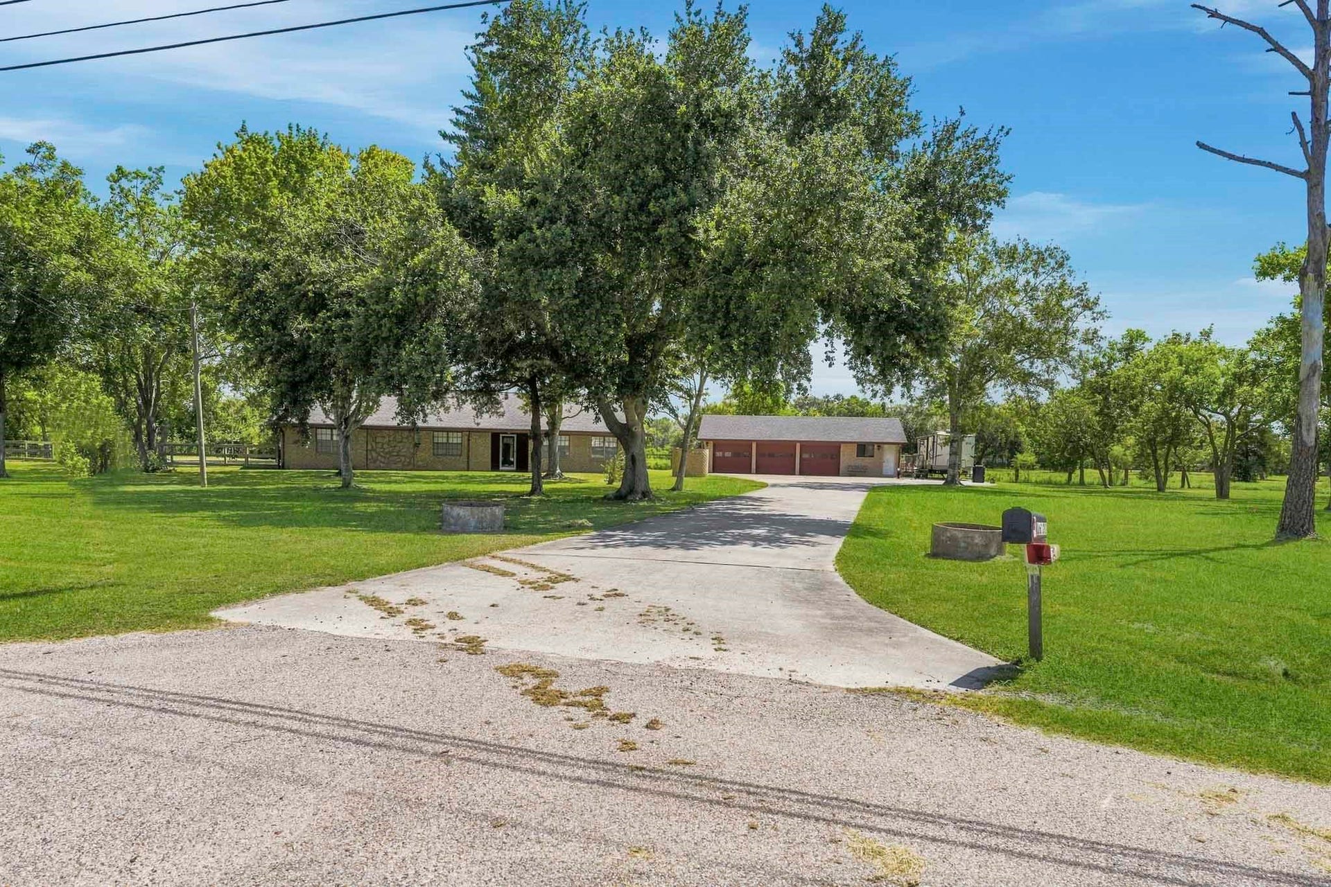 16101 Bluebird Street, Santa Fe, TX 77517 Charming countryside home nestled among mature trees, featuring a spacious driveway leading to a detached multi-car garage, all set on expansive, lush green grounds.