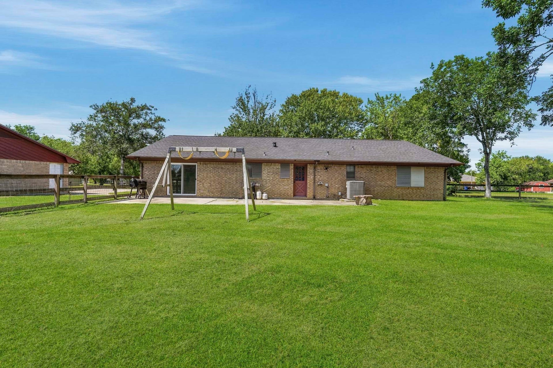 16101 Bluebird Street, Santa Fe, TX 77517 Charming brick home with a spacious backyard, perfect for outdoor activities, featuring a swing set and surrounded by lush greenery. Ideal for living and entertaining.
