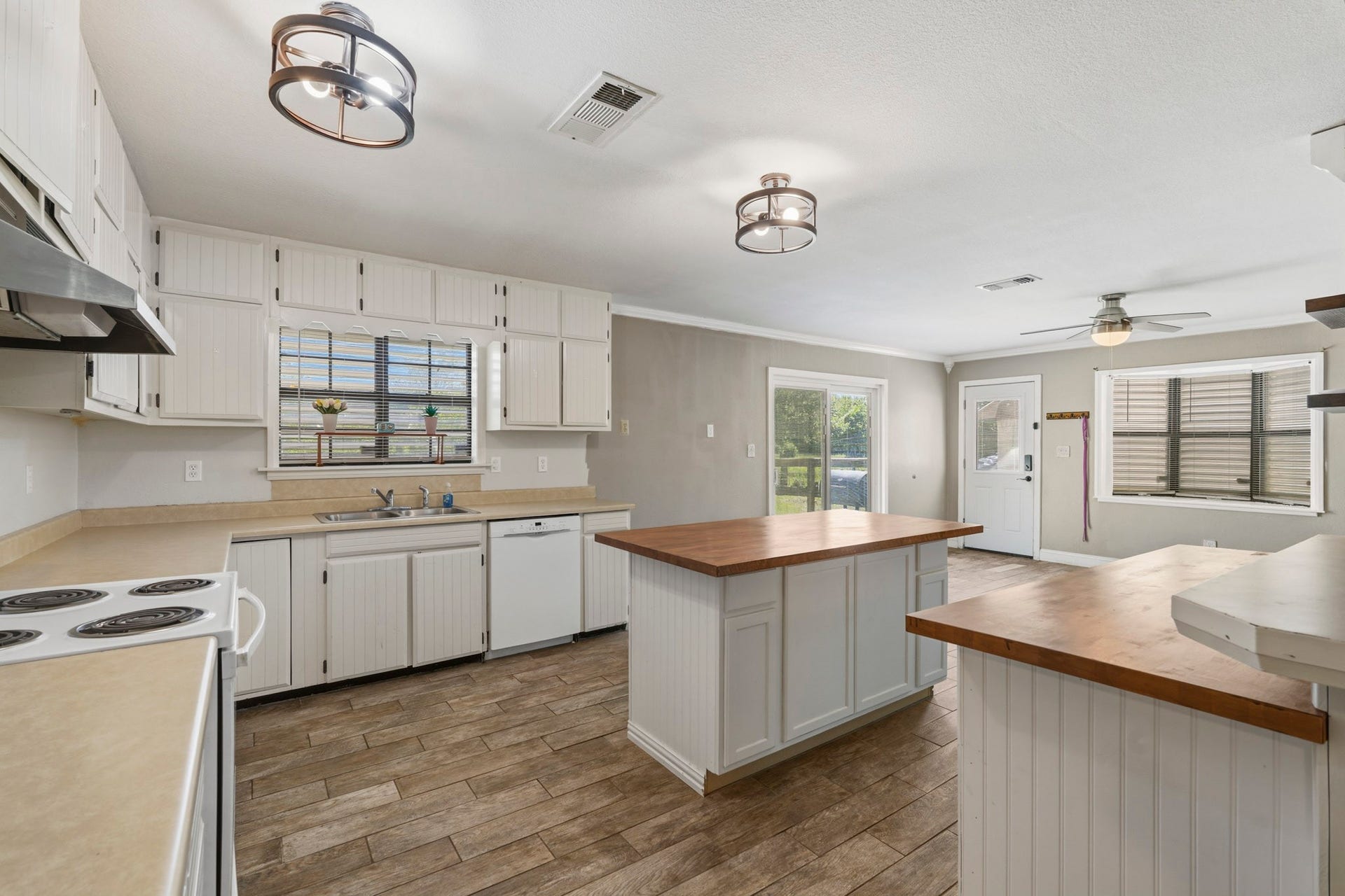 16101 Bluebird Street, Santa Fe, TX 77517 Spacious kitchen with rustic charm features wood-look tile flooring, ample cabinetry, and a central island with wood counter-top complemented by modern lighting and natural light from large windows.