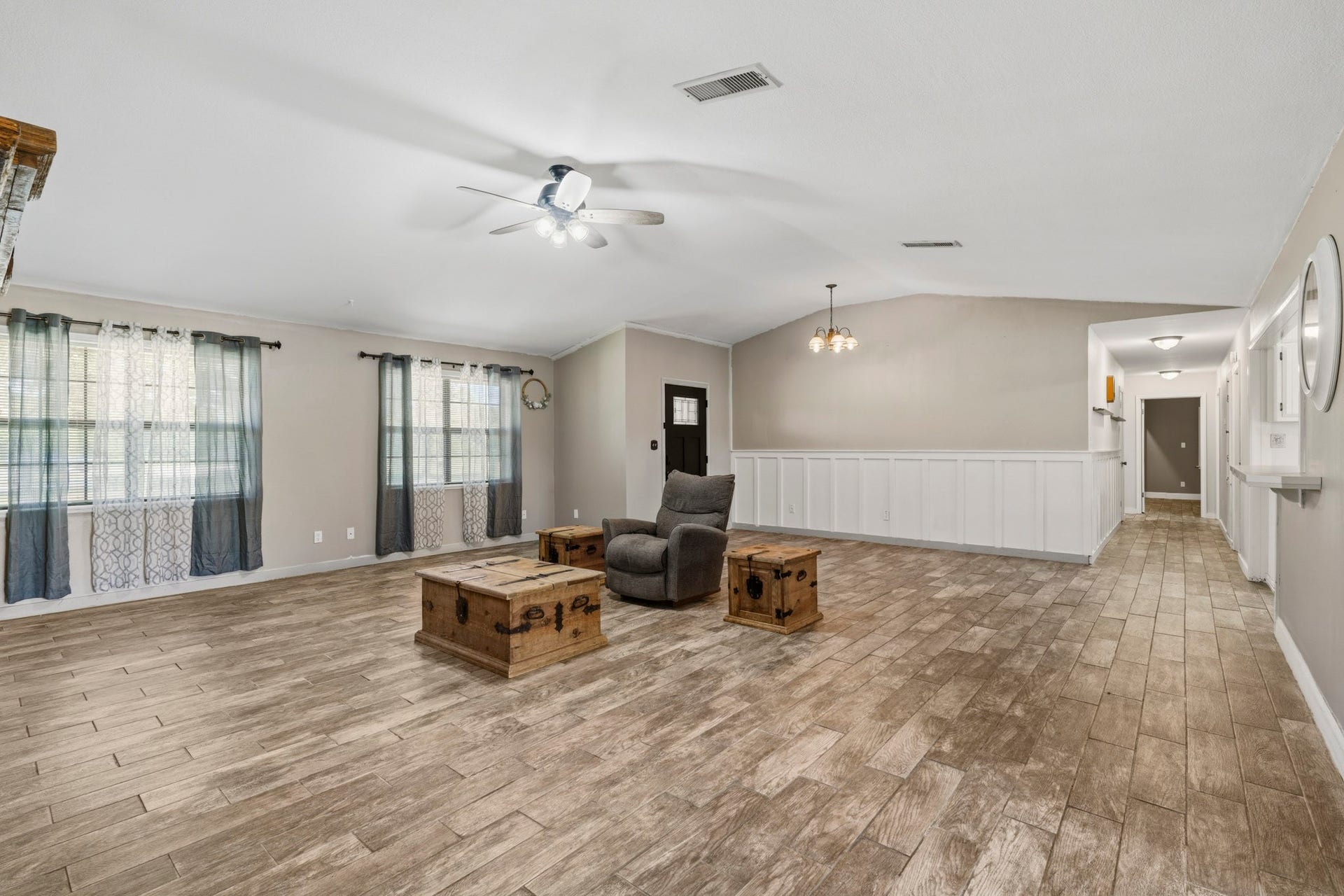 16101 Bluebird Street, Santa Fe, TX 77517 Spacious living area with elegant wood-look flooring, abundant natural light from large windows, and stylish wainscoting, creating an inviting atmosphere perfect for relaxation and entertainment.