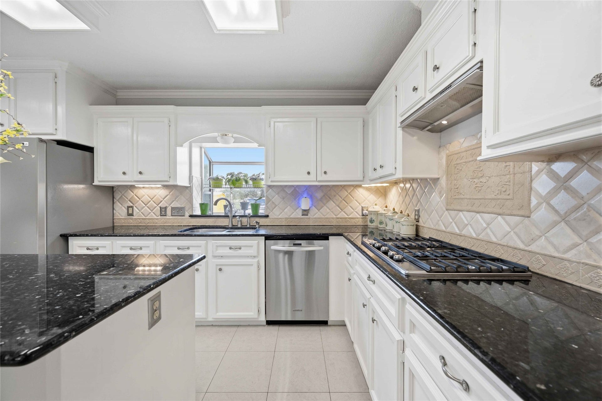 12075 Fm 359 Road, Hempstead, TX 77445 This modern kitchen features sleek white cabinetry, a central island with dark granite countertops, and stainless steel appliances. Bright, natural light fills the space, highlighting the elegant tiled backsplash and spacious layout. Perfect for both cooking and entertaining.