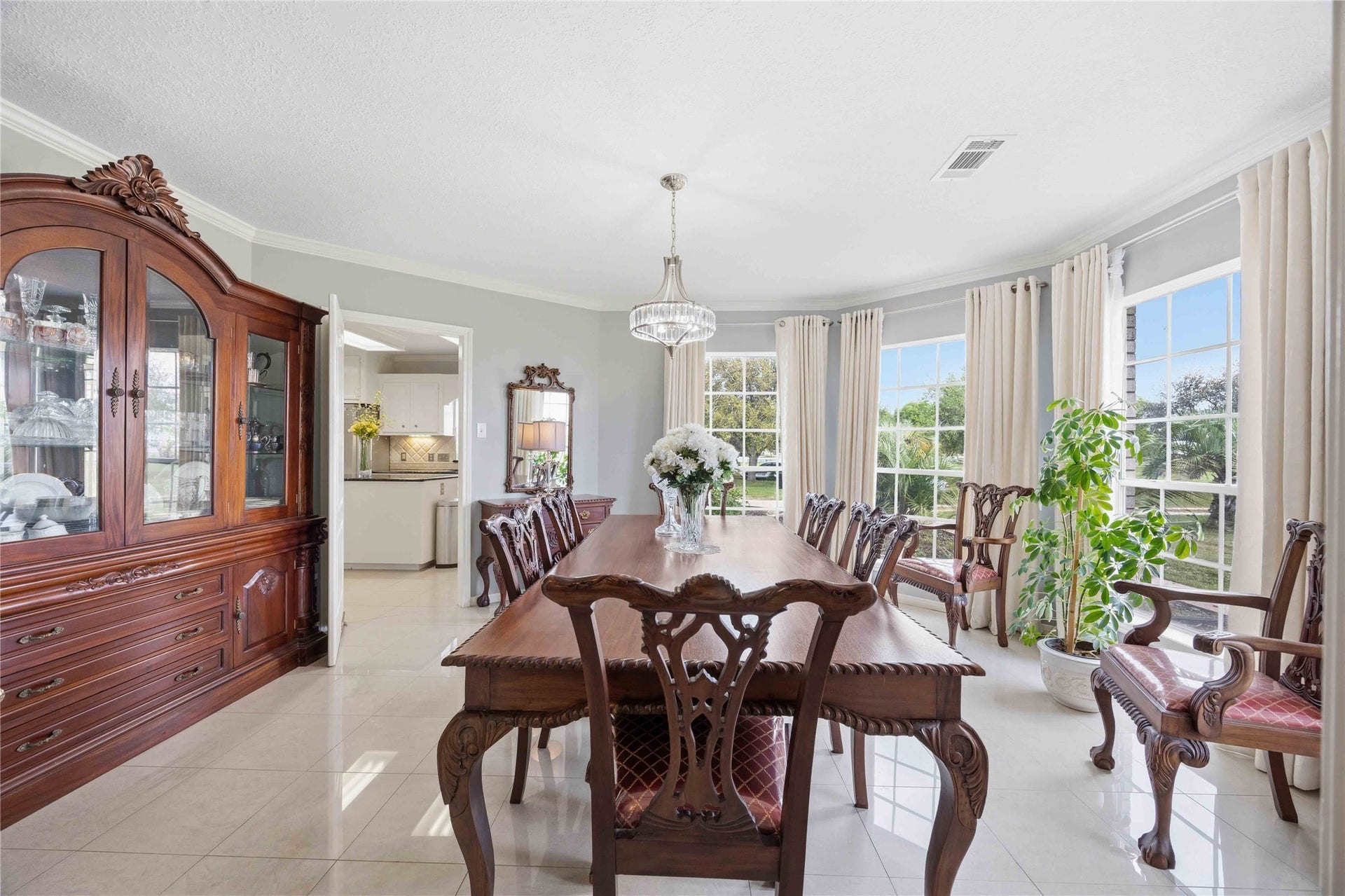 12075 Fm 359 Road, Hempstead, TX 77445 Elegant dining room with large windows providing ample natural light. Features a classic wooden table set, matching china cabinet, and polished tile flooring. Neutral tones create a bright and inviting atmosphere with a view of lush greenery outside.