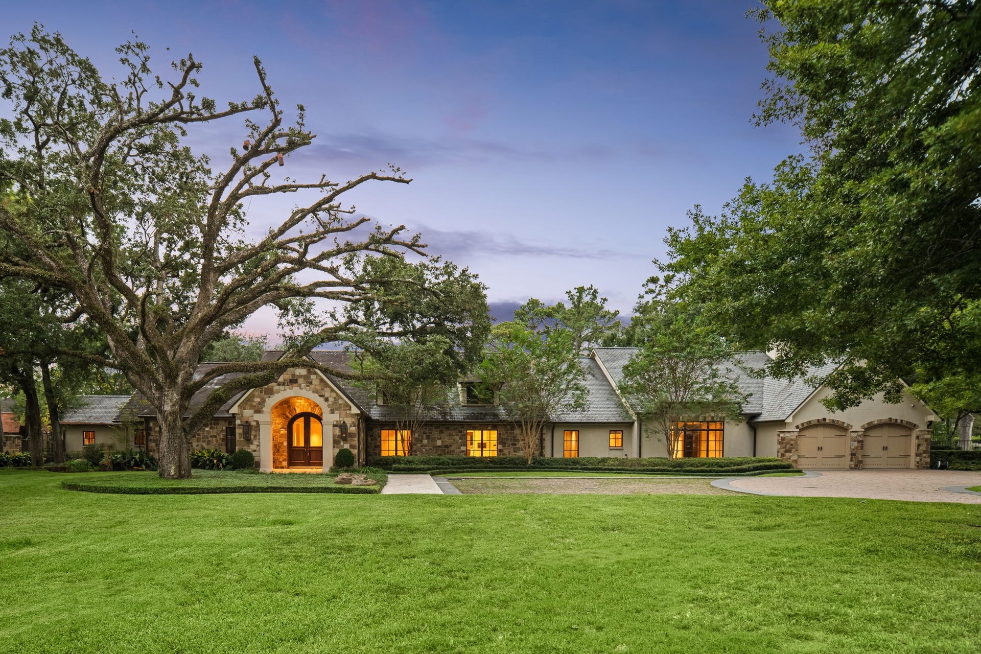 1 Gage Court, Houston, TX 77024 A broad manicured lawn, mature live oak and established landscaping frame the custom stone-and-stucco residence beneath a slate roof with copper gutters. The front elevation also showcases the arched entry, expansive motor court, attached two-car garage and privacy of the fully gated setting.