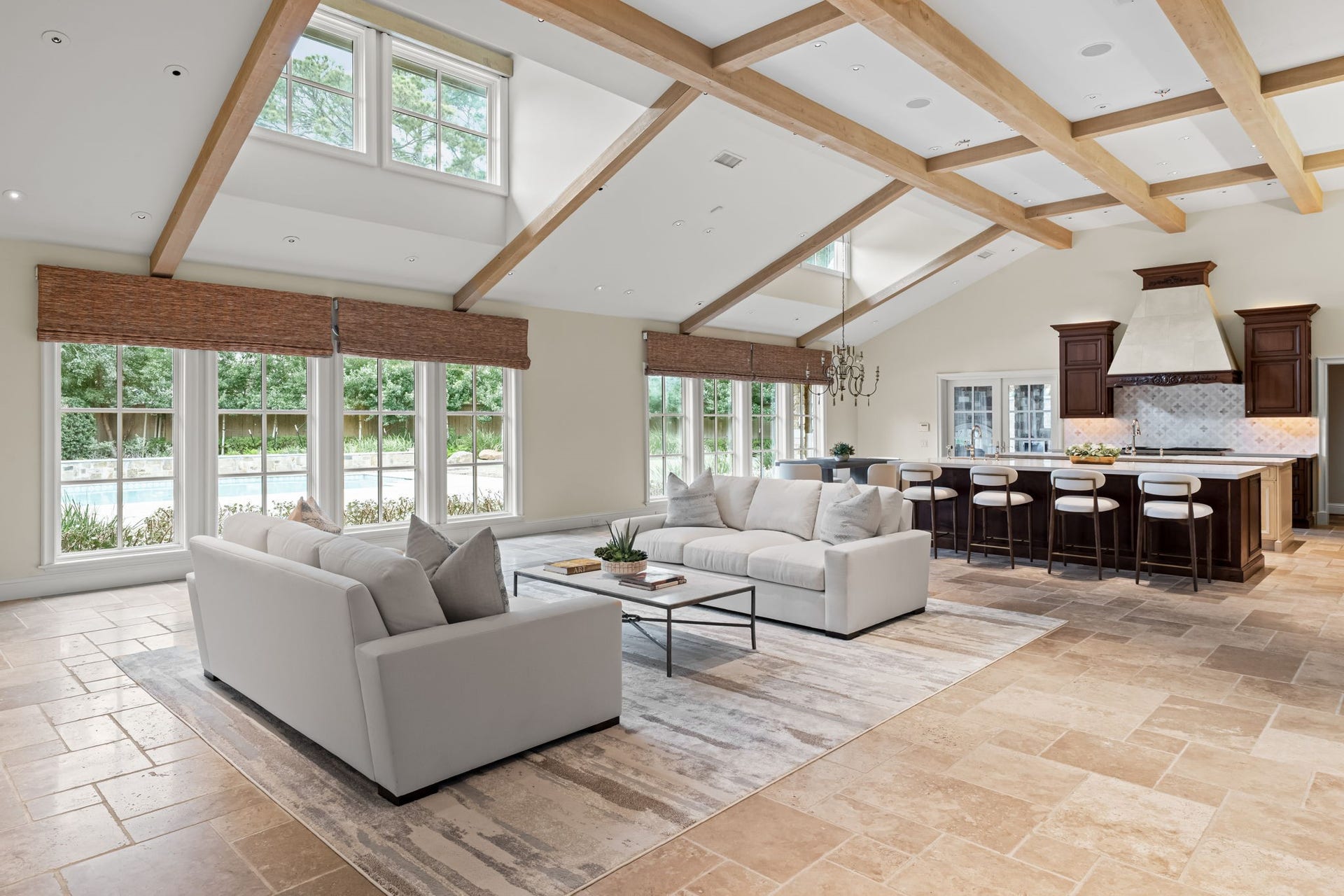 1 Gage Court, Houston, TX 77024 The great room showcases chiseled-edge travertine flooring beneath a dramatic vaulted ceiling with exposed wood beams and trusses. Expansive windows flood the room with natural light and frame views toward the backyard and pool.