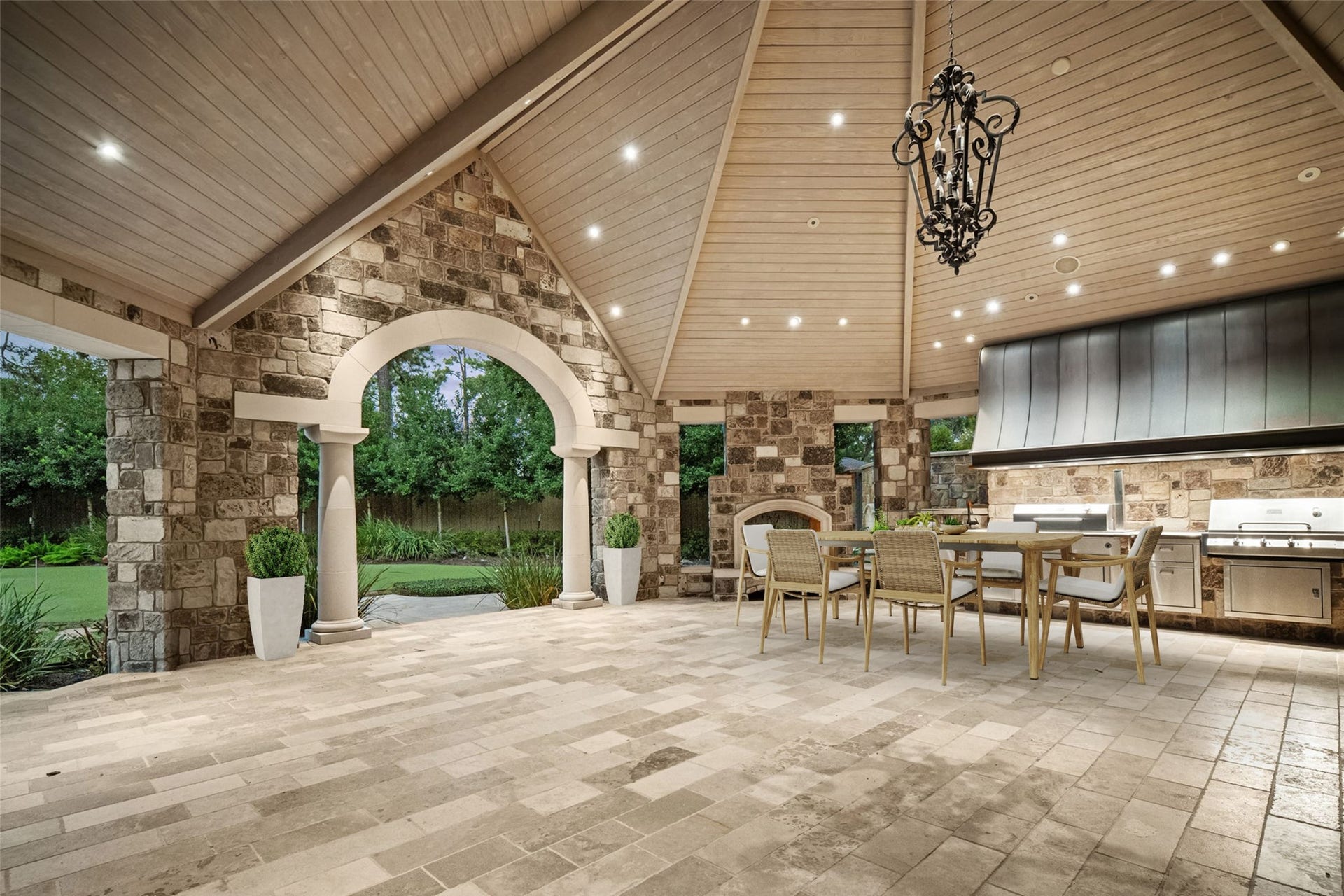 1 Gage Court, Houston, TX 77024 This view highlights the pavilions vaulted architecture, substantial stonework and custom copper vent hood within the summer kitchen. Lantern-style lighting and the large arched opening give the space the feel of a true outdoor room rather than a typical covered patio. (digitally staged)