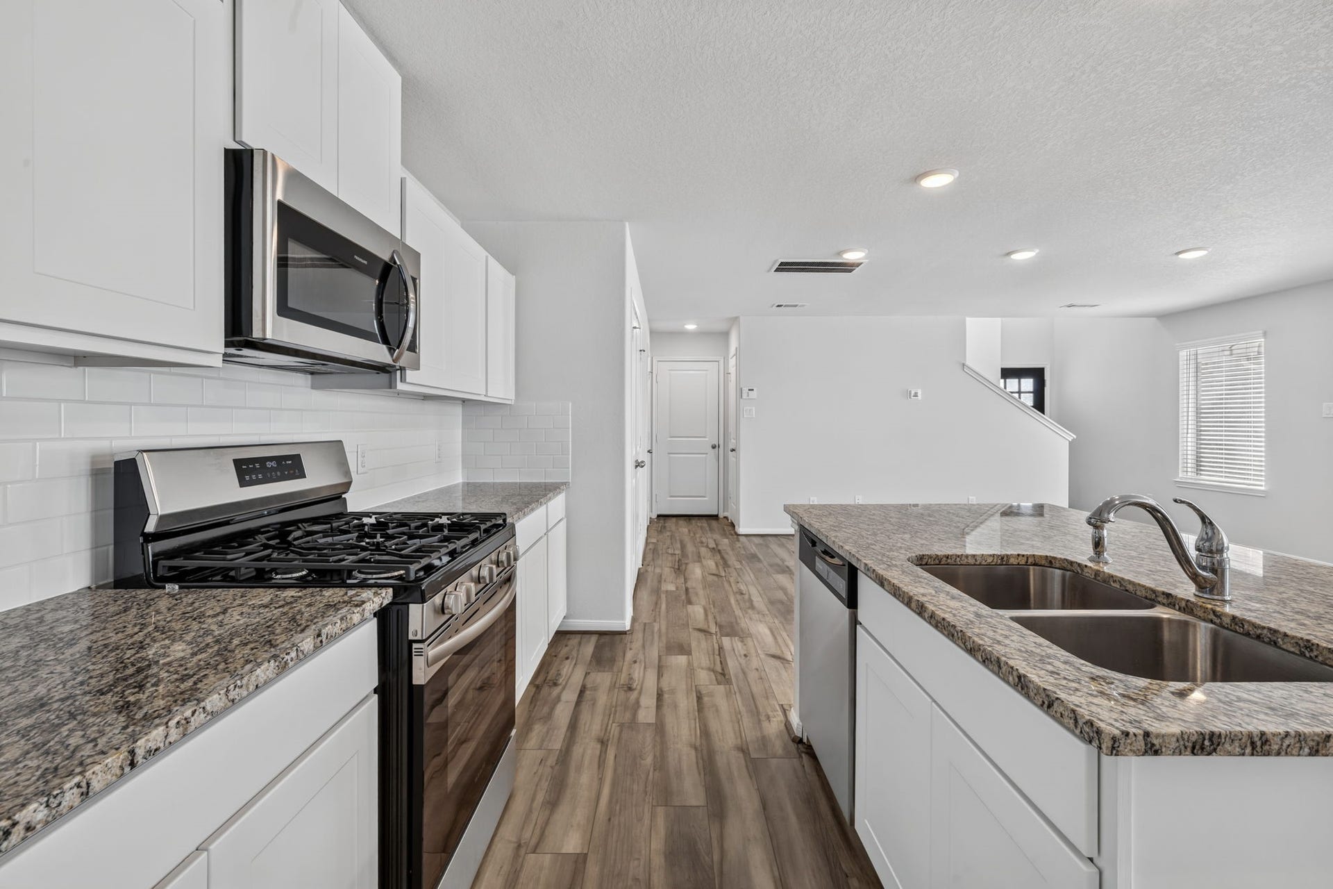 5243 Shallowhurst Lane, Katy, TX 77449 KITCHEN III - The gas range sits beneath a built-in microwave, with plenty of granite counter space and a view through the home toward the stairs, front entry and garage entry.