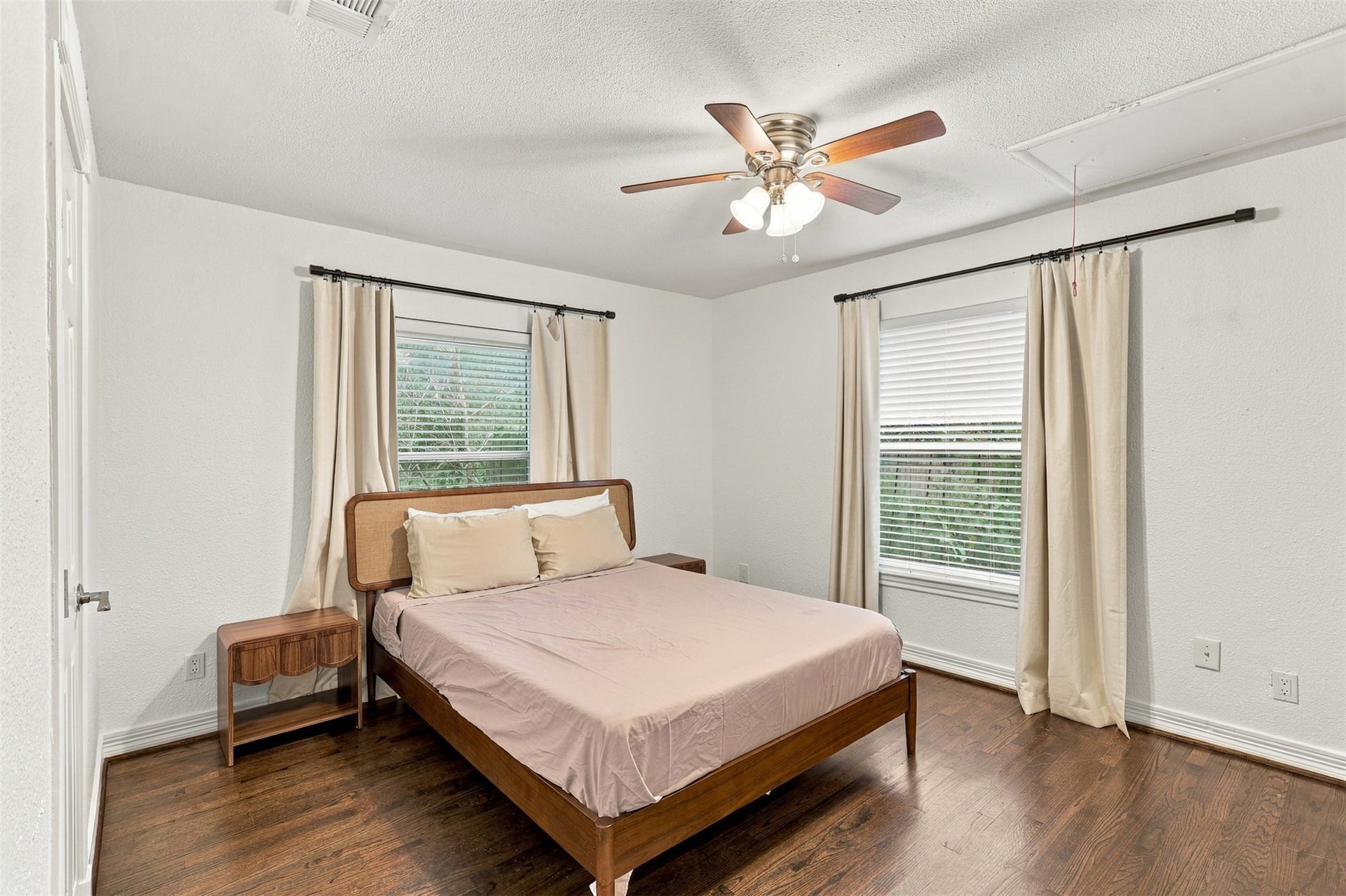 5410 Kiam Street, Houston, TX 77007 Bright and inviting bedroom with hardwood floors, featuring a comfortable bed, dual windows for natural light, and a ceiling fan for added comfort.