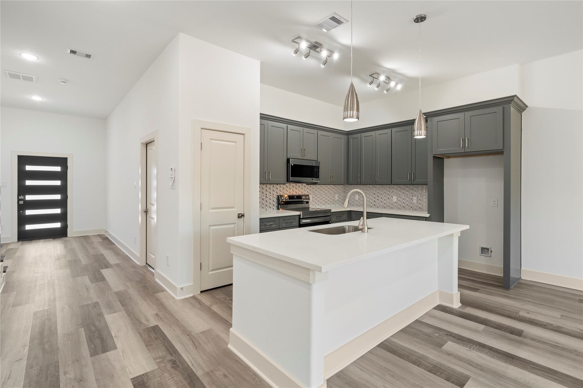 5629 Malmedy Road, Houston, TX 77033 Modern kitchen with sleek gray cabinetry, stainless steel appliances, and a spacious island with pendant lighting, seamlessly connected to an open living area with stylish flooring.