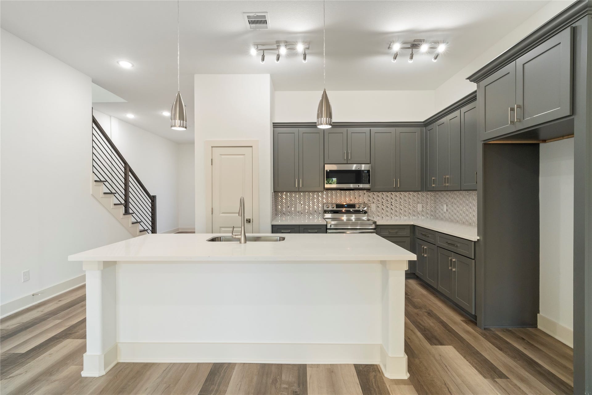 5629 Malmedy Road, Houston, TX 77033 Stylish modern kitchen featuring sleek gray cabinetry, a spacious island with a sink, stainless steel appliances, and elegant pendant lighting.