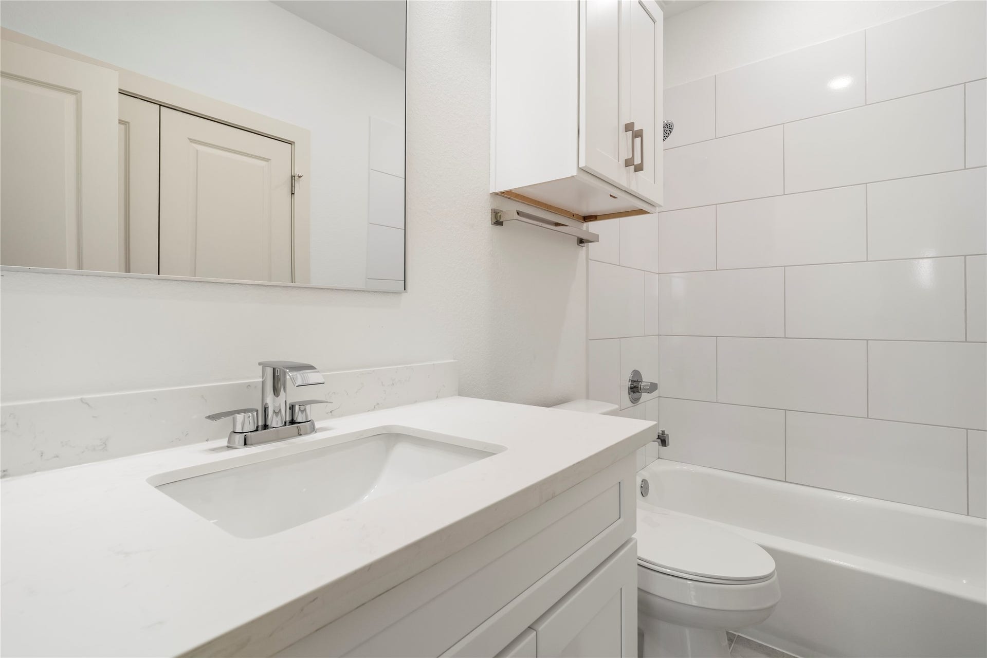 5629 Malmedy Road, Houston, TX 77033 Sleek and modern bathroom featuring a spacious vanity with a white countertop, elegant fixtures, and a pristine tub-shower combo with stylish white tile accents.
