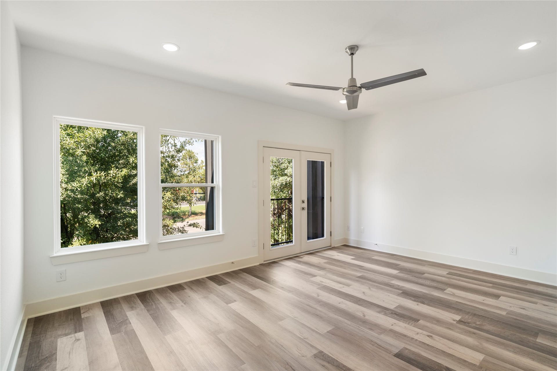 5629 Malmedy Road, Houston, TX 77033 Bright and airy primary bedroom featuring large windows, elegant wood flooring, and a ceiling fan, with glass doors leading to a serene outdoor view.