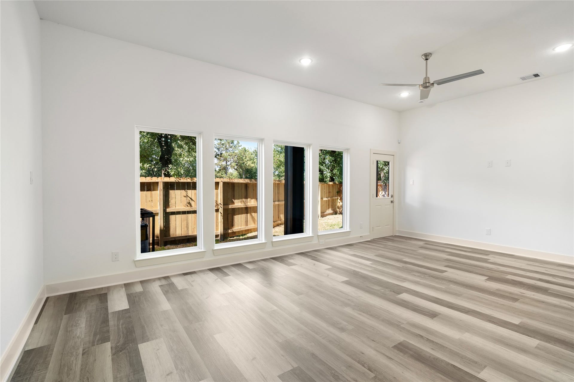 5629 Malmedy Road, Houston, TX 77033 Bright and spacious living room with large windows, modern gray flooring, and a ceiling fan, offering a seamless connection to the outdoors through a glass door.