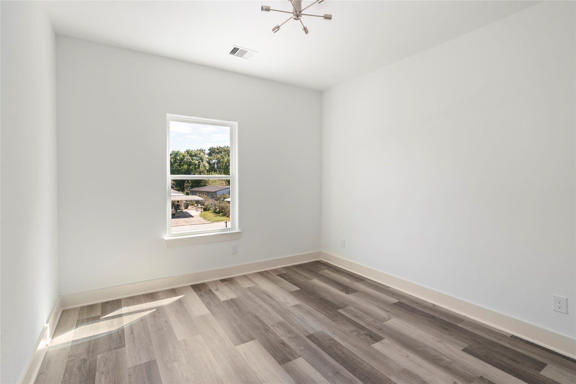 5629 Malmedy Road, Houston, TX 77033 Bright and airy room featuring modern wood-look flooring, a large window for natural light, and a sleek, contemporary ceiling light fixture.