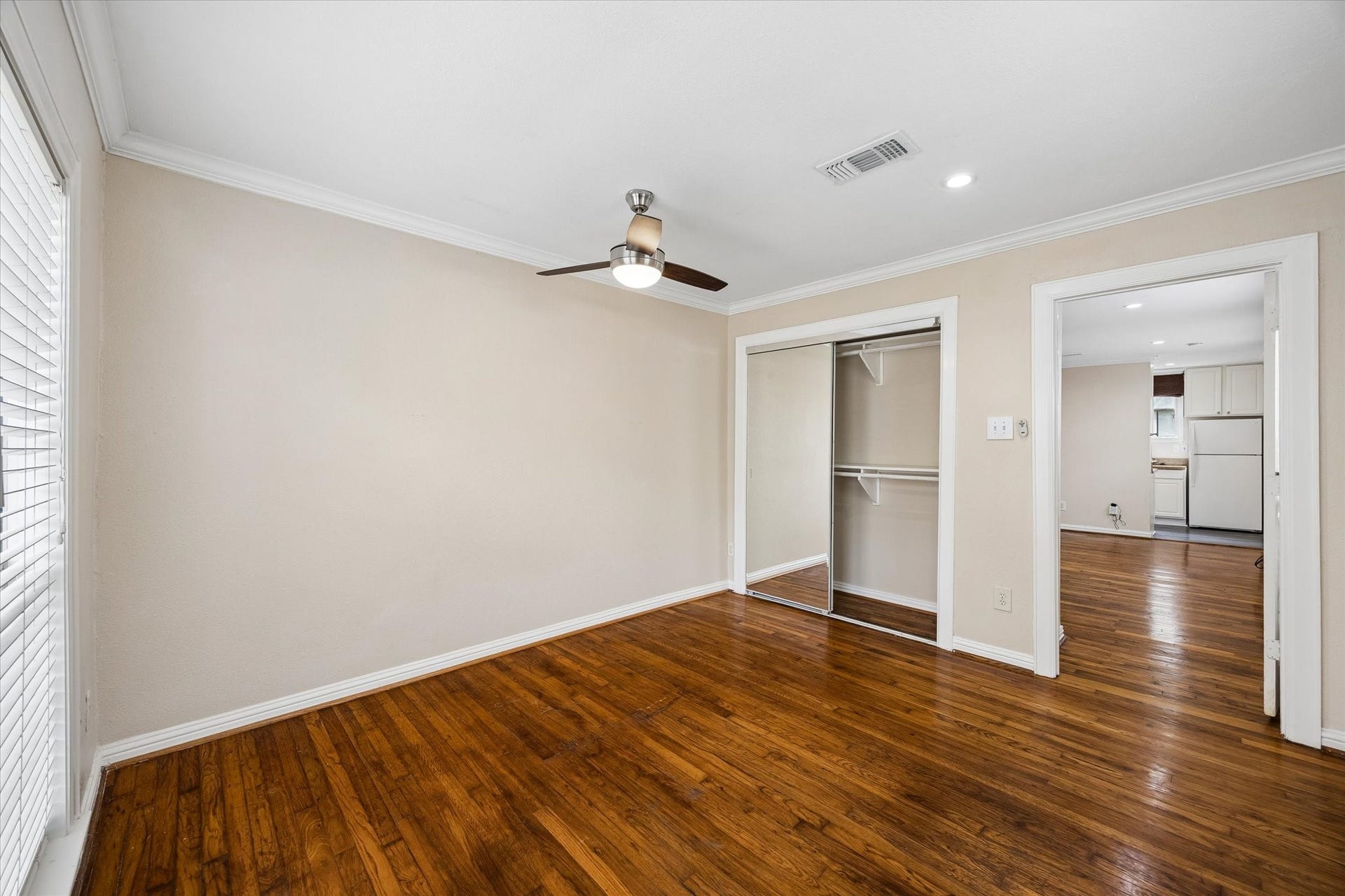 1020 Crocker Street, Houston, TX 77019 Bright room with hardwood floors, a ceiling fan, and a mirrored closet, leading into a kitchen area.