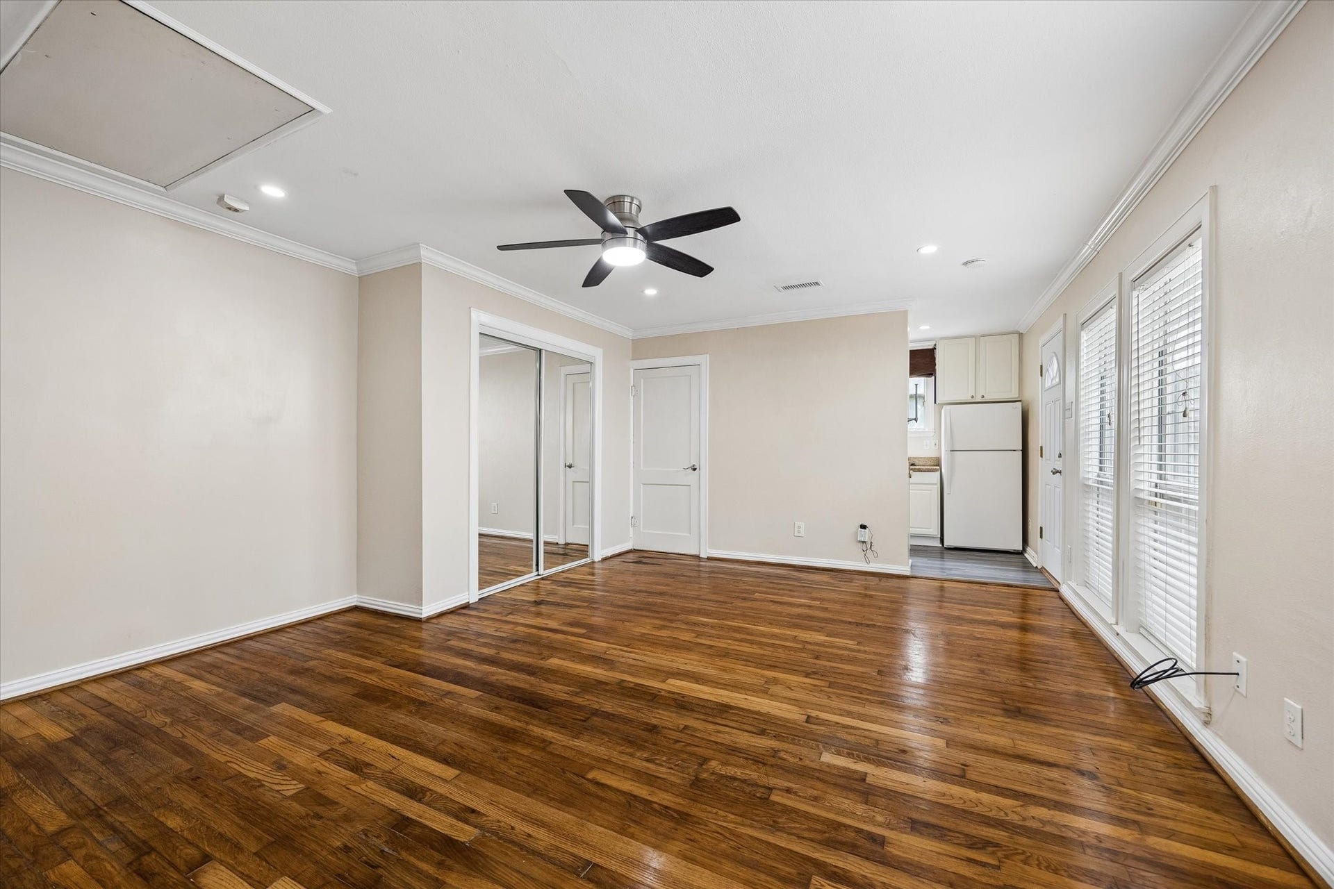 1020 Crocker Street, Houston, TX 77019 Spacious living area featuring rich hardwood floors, a modern ceiling fan, and ample natural light from large windows. The room seamlessly connects to a cozy kitchen with white cabinetry and appliances.