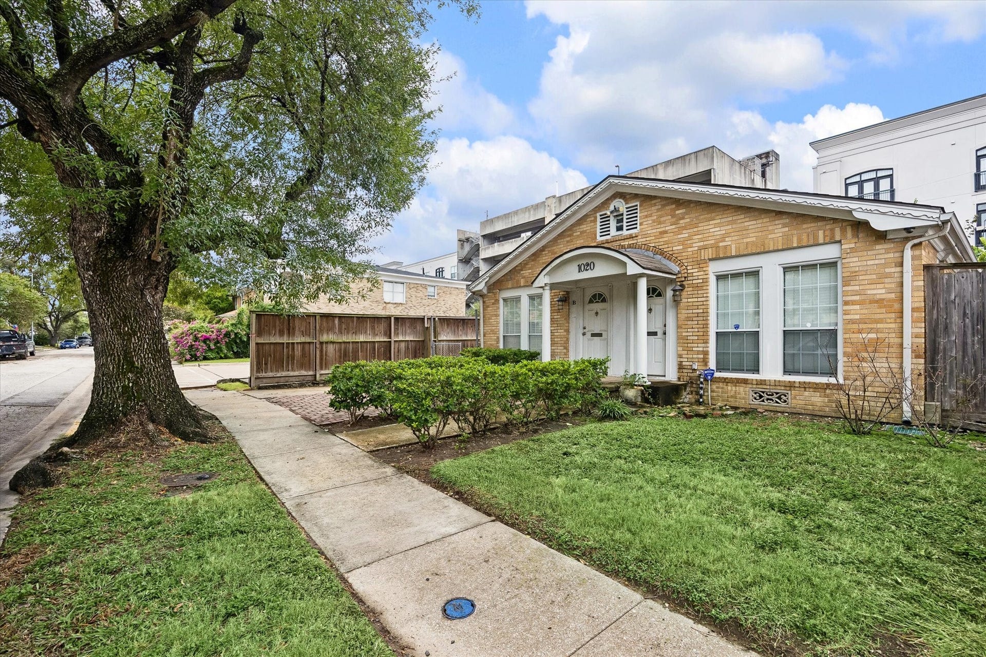 1020 Crocker Street, Houston, TX 77019 Charming brick home with a welcoming front porch, lush greenery, and mature trees, offering a cozy and inviting atmosphere.