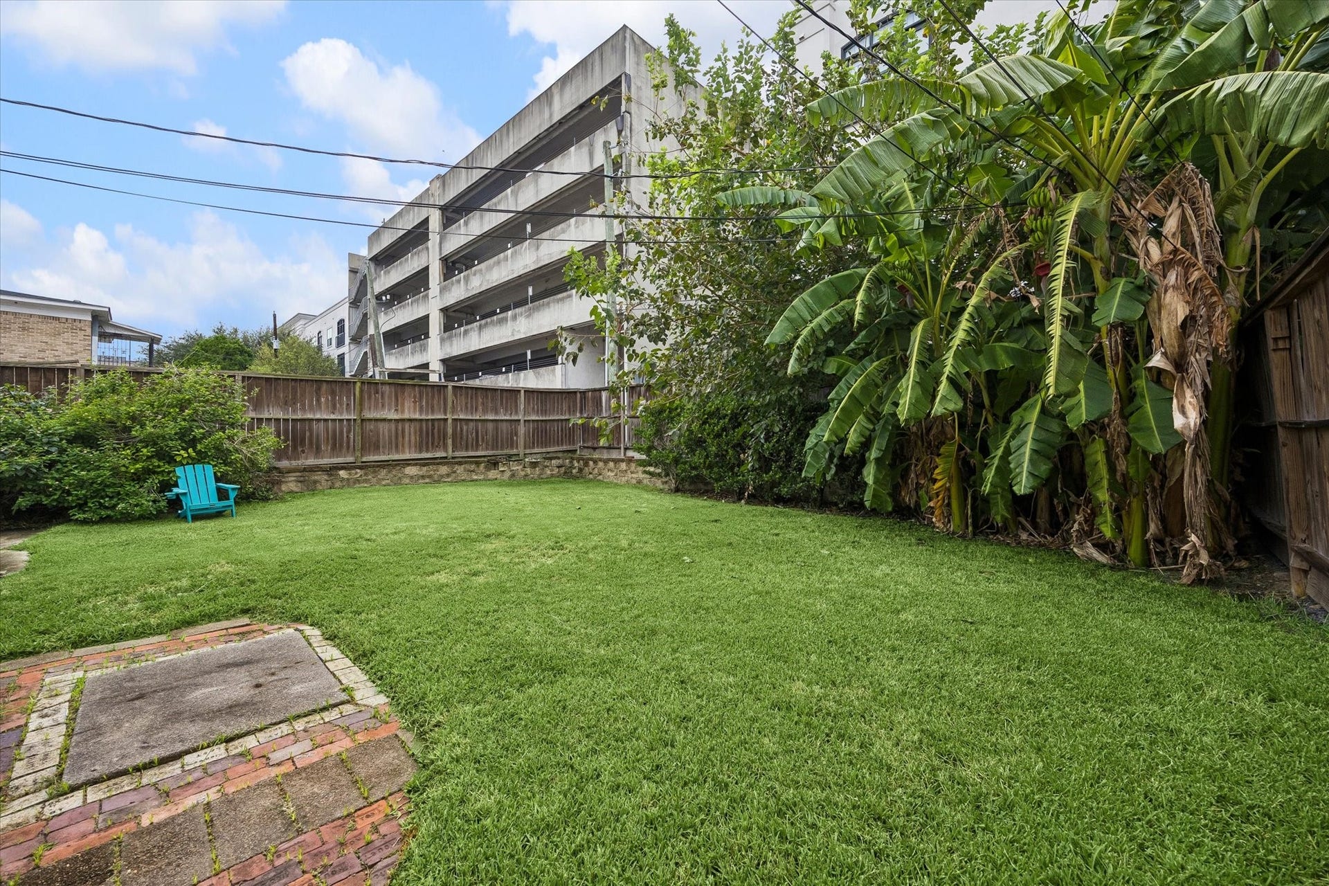 1020 Crocker Street, Houston, TX 77019 Spacious backyard oasis with lush green lawn, tropical plants, and a charming brick patio, perfect for relaxing and entertaining.