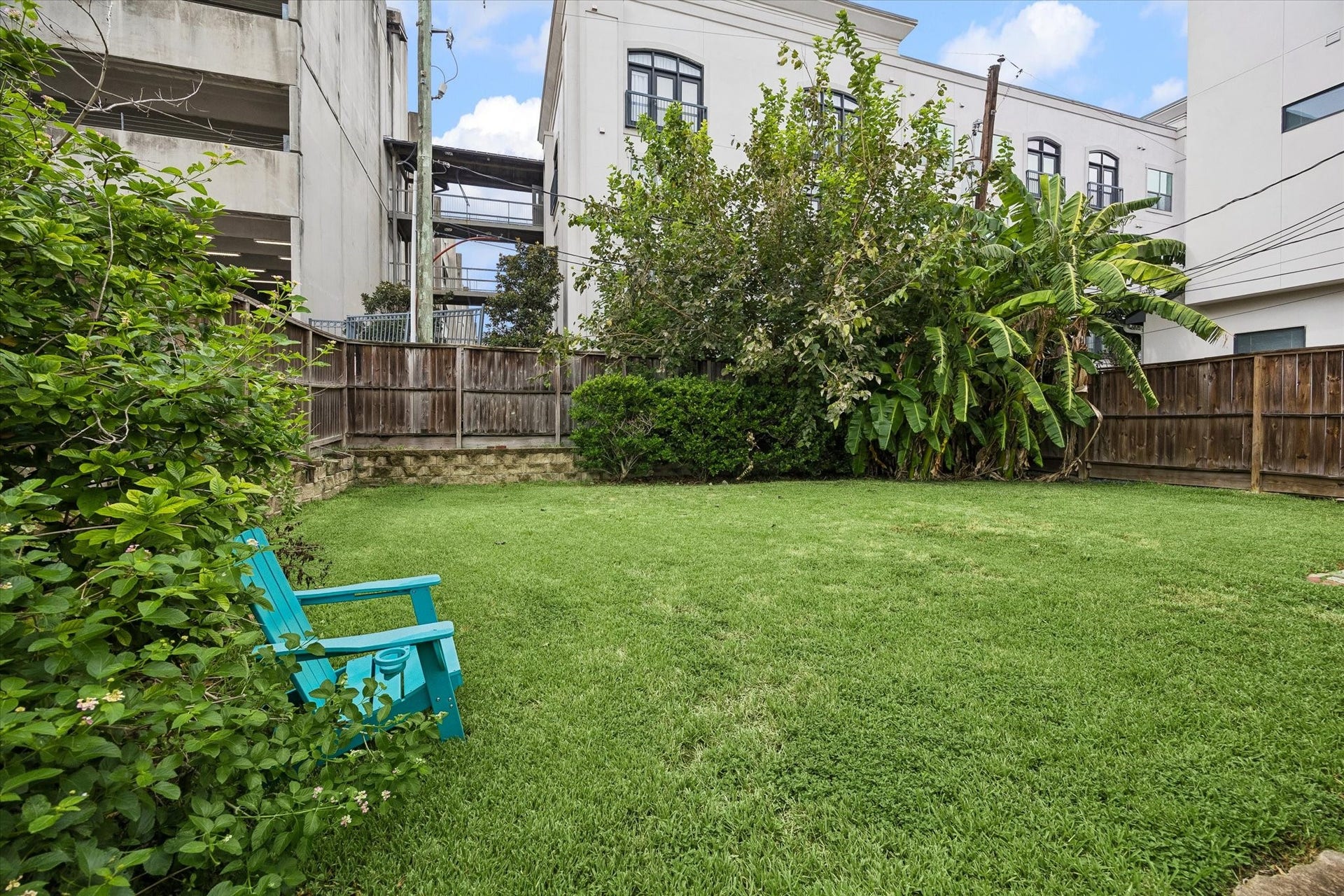 1020 Crocker Street, Houston, TX 77019 Charming backyard oasis with lush greenery, a vibrant turquoise chair, and privacy fencing, perfect for relaxation and outdoor gatherings.