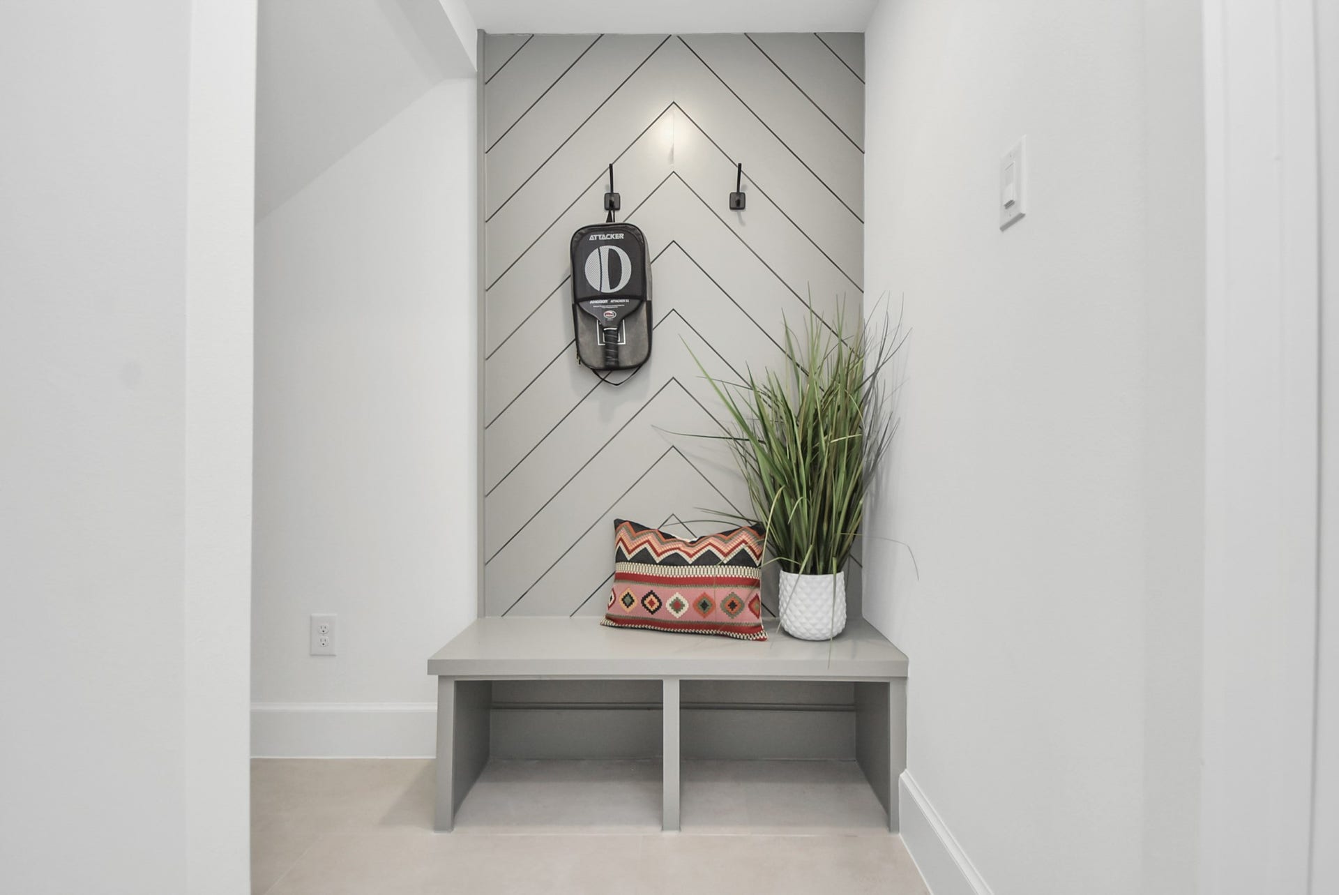 927 Fisher Street, #B, Houston, TX 77018 Step into this modern, minimalist nook featuring a sleek bench against chevron-patterned wall paneling. Accented with a decorative pillow and a potted plant, this space combines style and functionality, making it an inviting entryway or practical mudroom for everyday living.