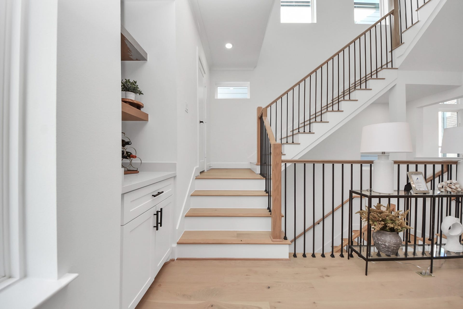 927 Fisher Street, #B, Houston, TX 77018 Ascend this bright, modern staircase with wooden steps and sleek metal railings. A built-in cabinet with open shelving and decorative touches like plants and a lamp create a welcoming and stylish entryway.