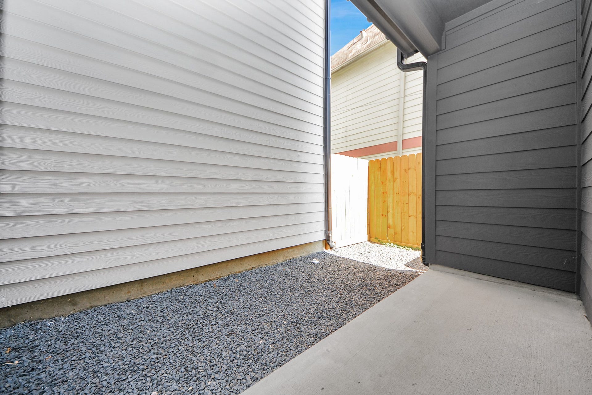 927 Fisher Street, #B, Houston, TX 77018 Step into this narrow outdoor side area between homes, with gravel ground and siding walls. A wooden fence at the end provides privacy while maintaining a clean and orderly appearance.