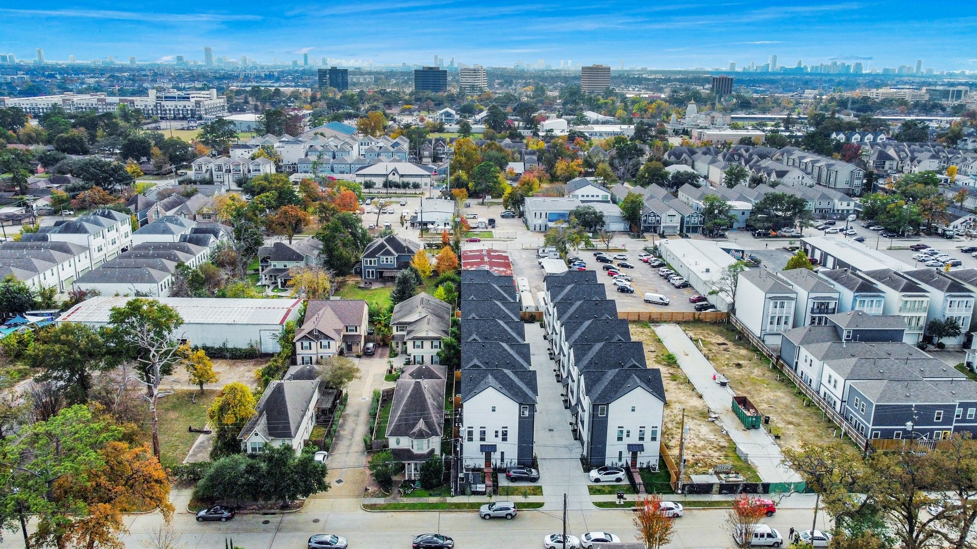 927 Fisher Street, #B, Houston, TX 77018 From above, this suburban neighborhood offers a mix of modern townhouses and traditional homes, surrounded by greenery and tree-lined streets. The distant city skyline emphasizes convenient access to urban amenities while maintaining a peaceful residential feel.