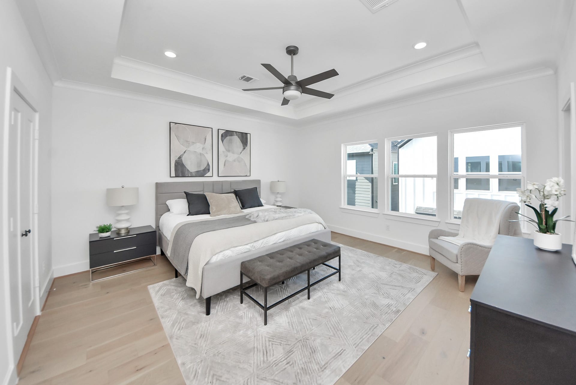 927 Fisher Street, #B, Houston, TX 77018 This spacious bedroom offers a serene retreat with a modern design, a large bed, and stylish furnishings. Natural light streams through multiple windows, highlighting the cozy seating area, ceiling fan, and light wood flooring for a bright, relaxing atmosphere.