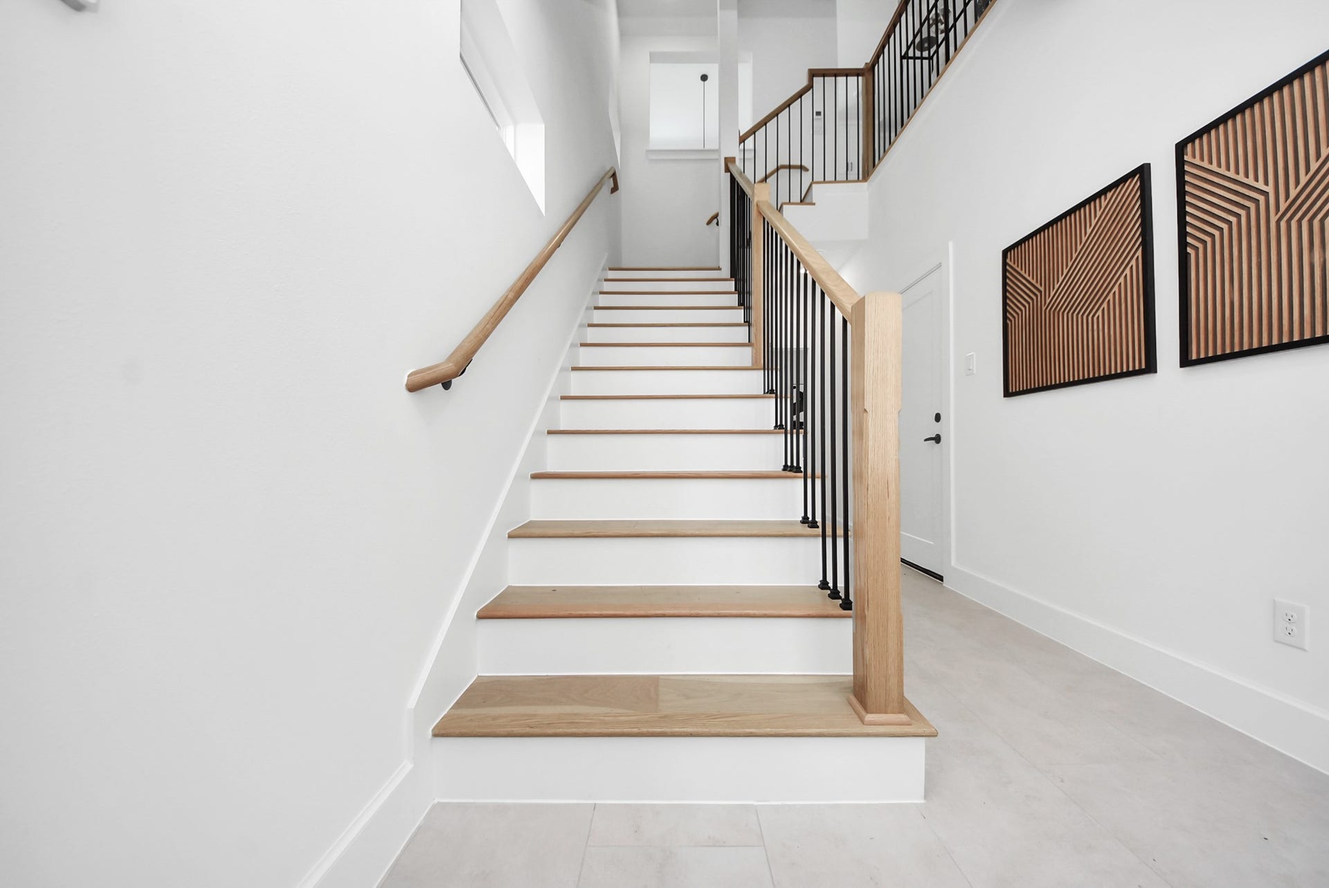 927 Fisher Street, #B, Houston, TX 77018 Ascend this modern staircase with light wood steps and sleek black metal railings, set against bright white walls. Geometric wall art adds a contemporary touch, creating an inviting transition between the homes levels while highlighting its clean, modern design.