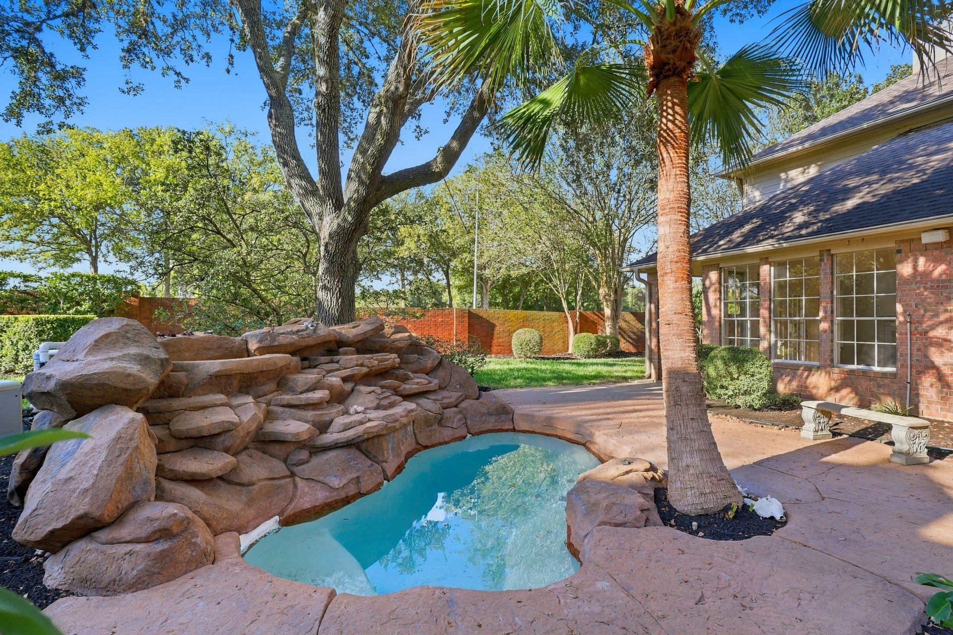 1931 Auburn Trail, Sugar Land, TX 77479 Charming backyard oasis featuring a natural rock waterfall cascading into a serene pool, surrounded by lush landscaping and mature trees for ultimate privacy and relaxation.