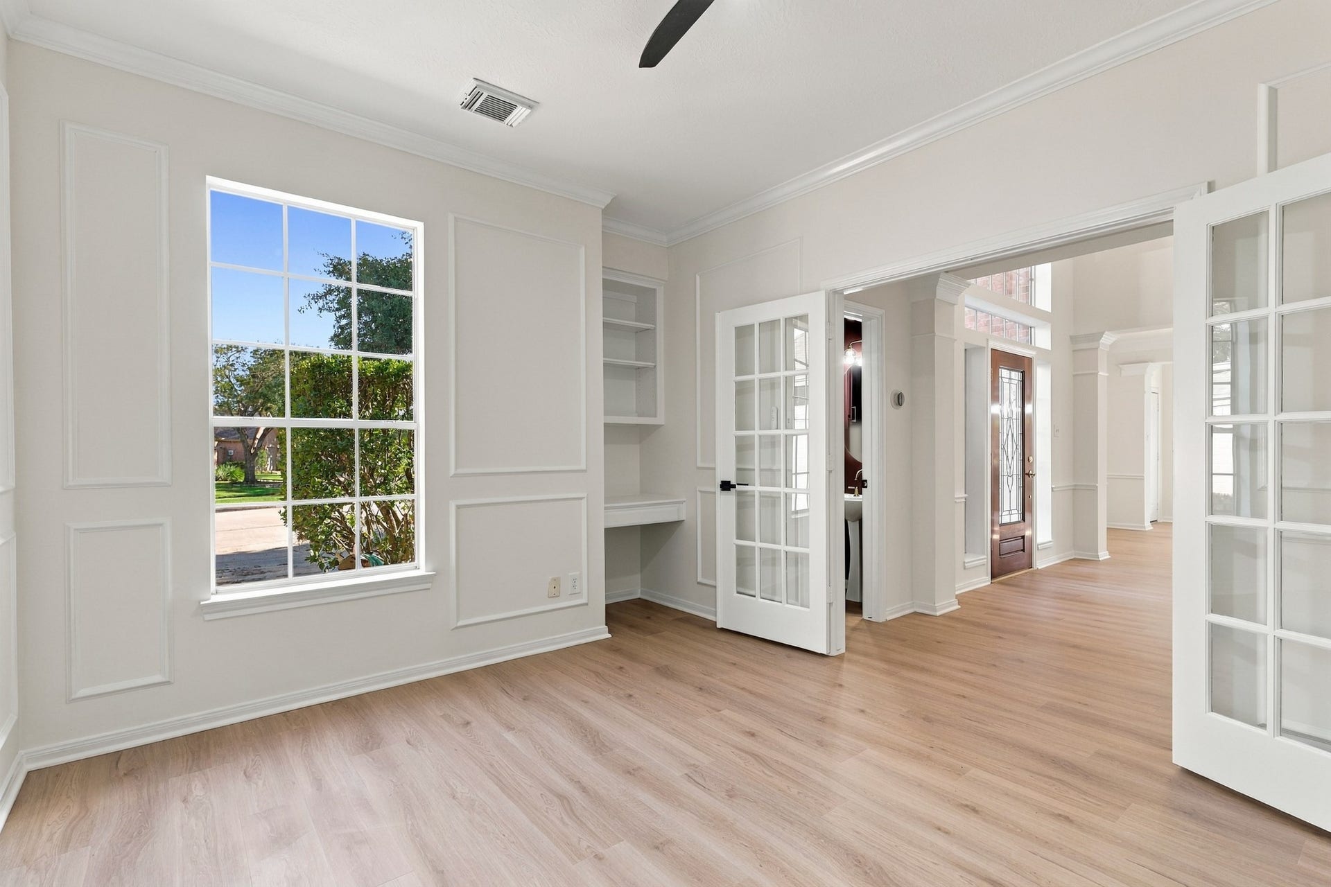 1931 Auburn Trail, Sugar Land, TX 77479 Bright and inviting home office with elegant French doors, built-in shelving, and abundant natural light from the large window, complementing the warm wood flooring.