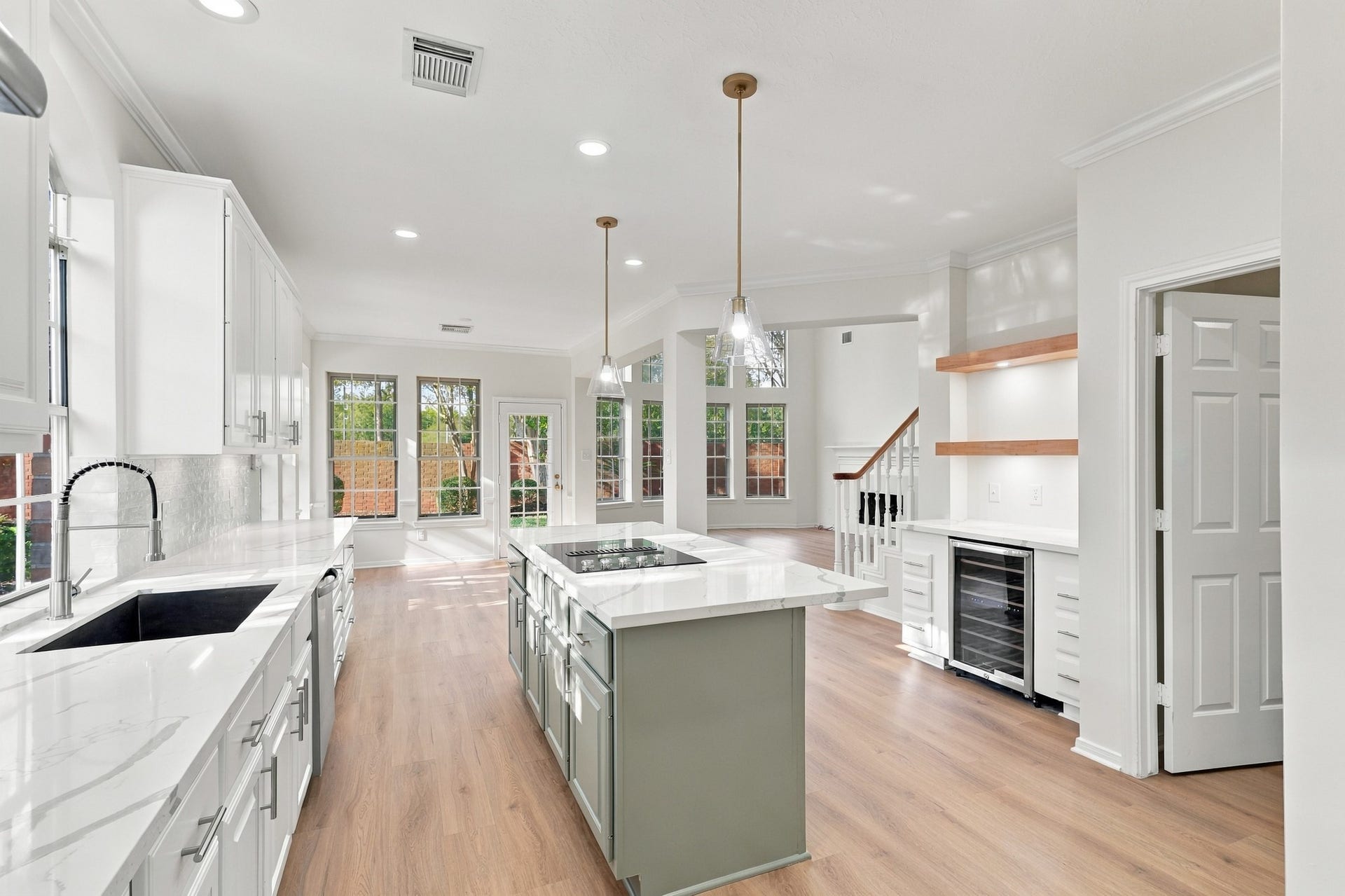1931 Auburn Trail, Sugar Land, TX 77479 Bright and spacious open-concept kitchen featuring elegant white cabinetry, a large island with a cooktop, and sleek pendant lighting, seamlessly flowing into a sunlit living area with large windows and hardwood floors.