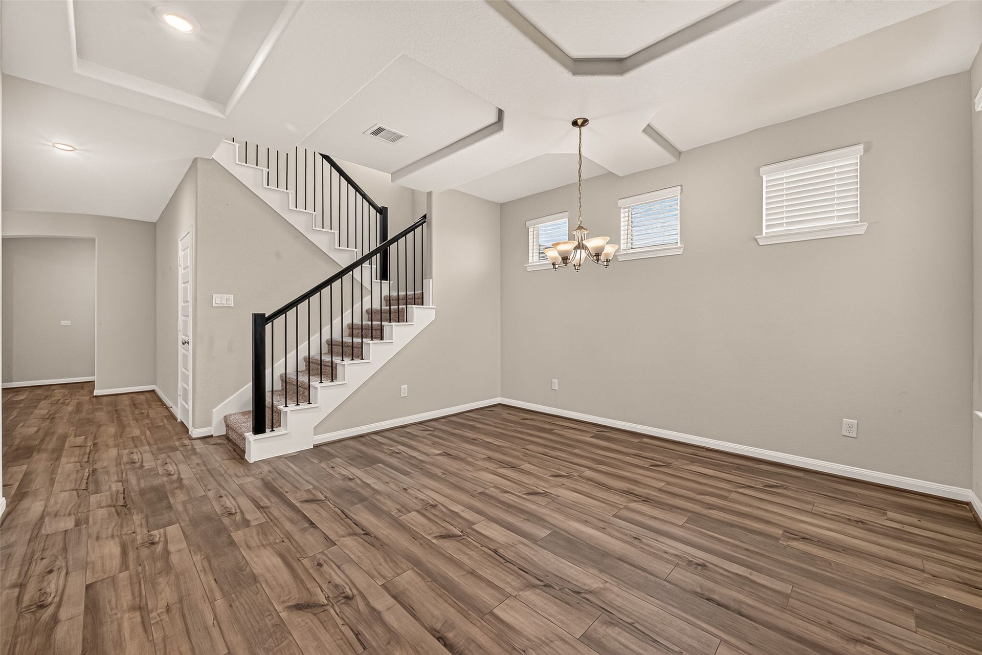 Elegant dining area with a modern chandelier is complemented by a stylish staircase and ample natural light from high windows.