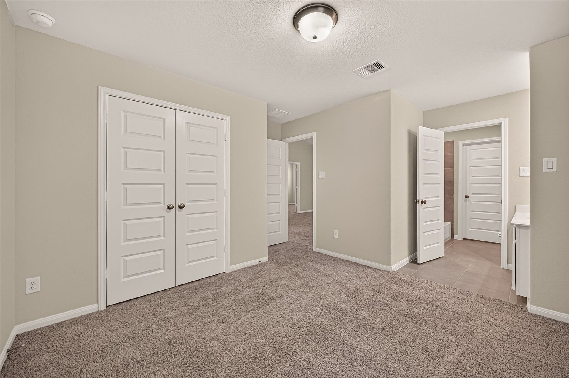 Spacious secondary bedroom with jack and jill bathroom access. Plush carpet, neutral walls, and ample closet space, featuring elegant white doors and a cozy, inviting atmosphere.