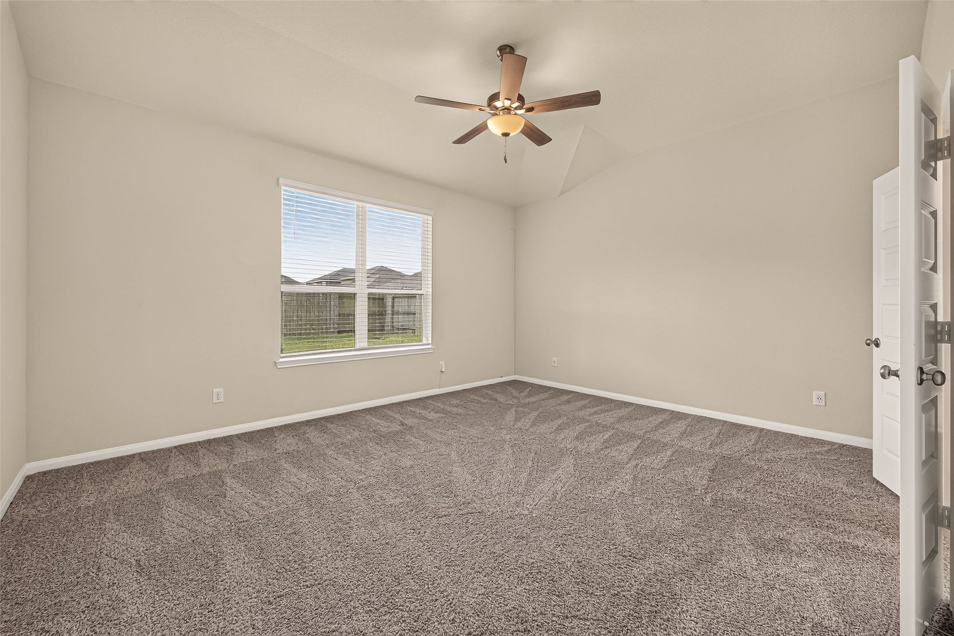 Spacious bedroom featuring plush carpet, a ceiling fan, and ample natural light from a large window overlooking the backyard.