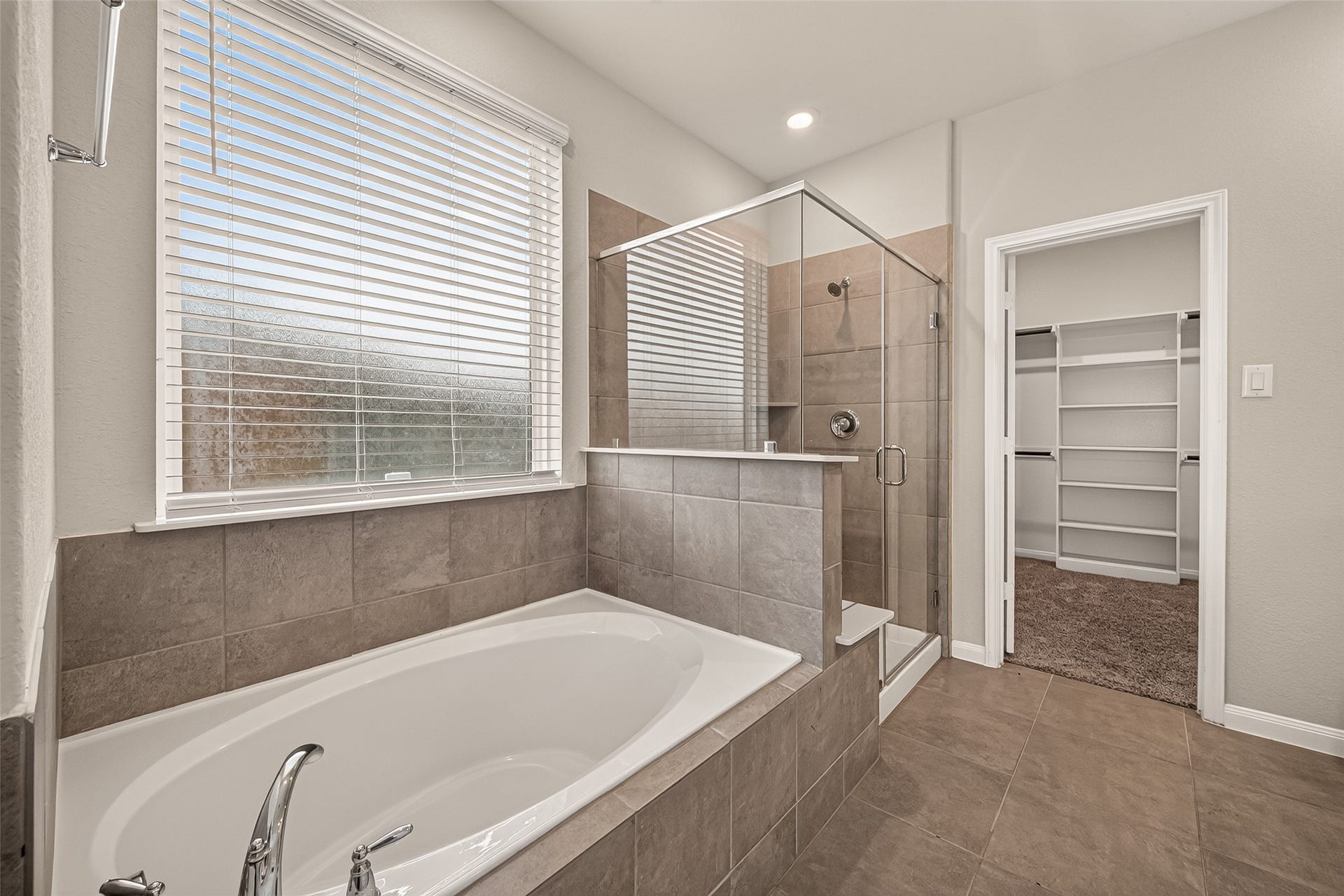 Luxurious bathroom featuring a spacious soaking tub and a sleek glass-enclosed shower, complemented by a walk-in closet for ample storage.