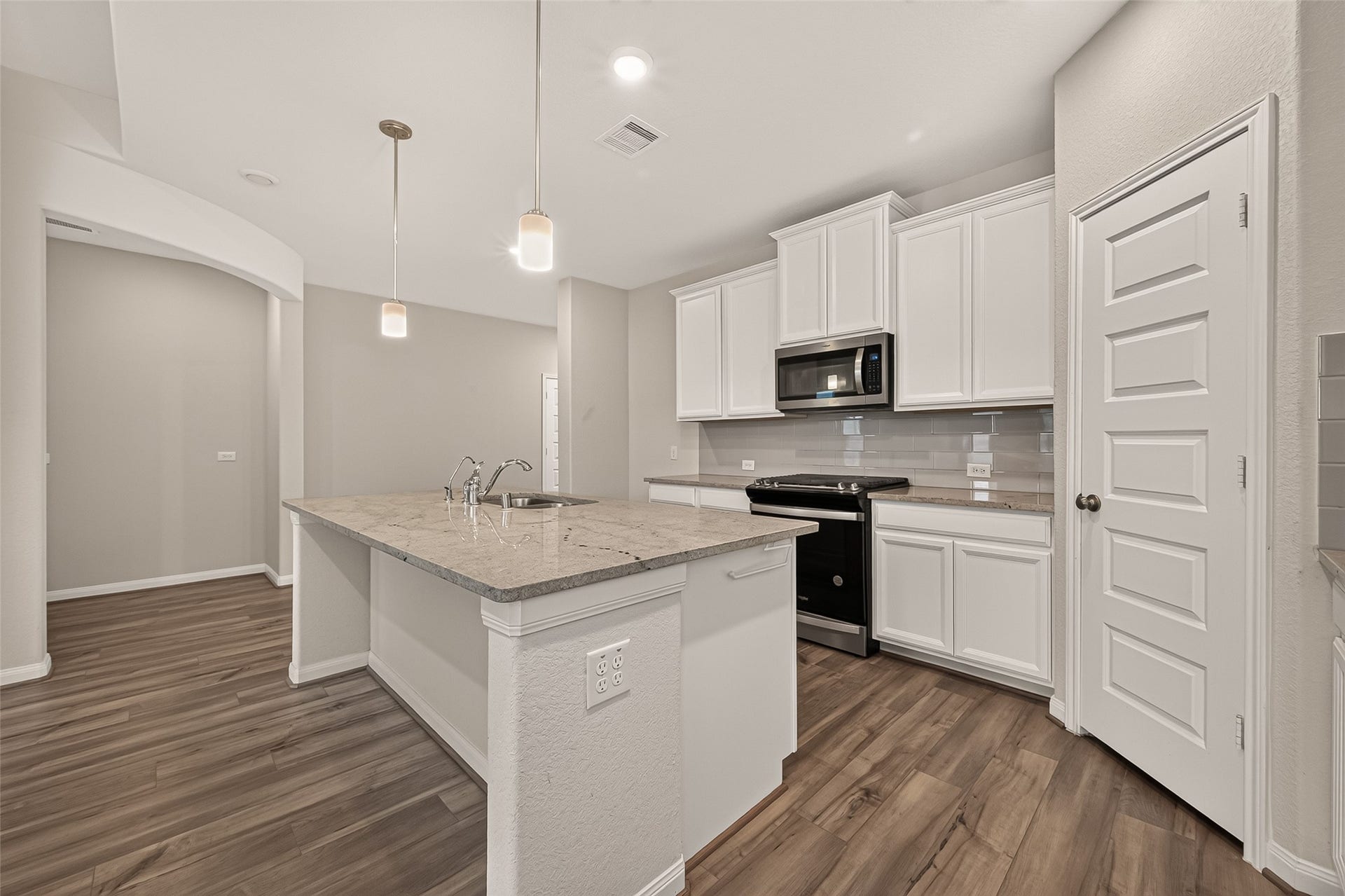 Elegant kitchen featuring sleek white cabinetry, a spacious island with granite countertops, modern appliances, and stylish flooring.