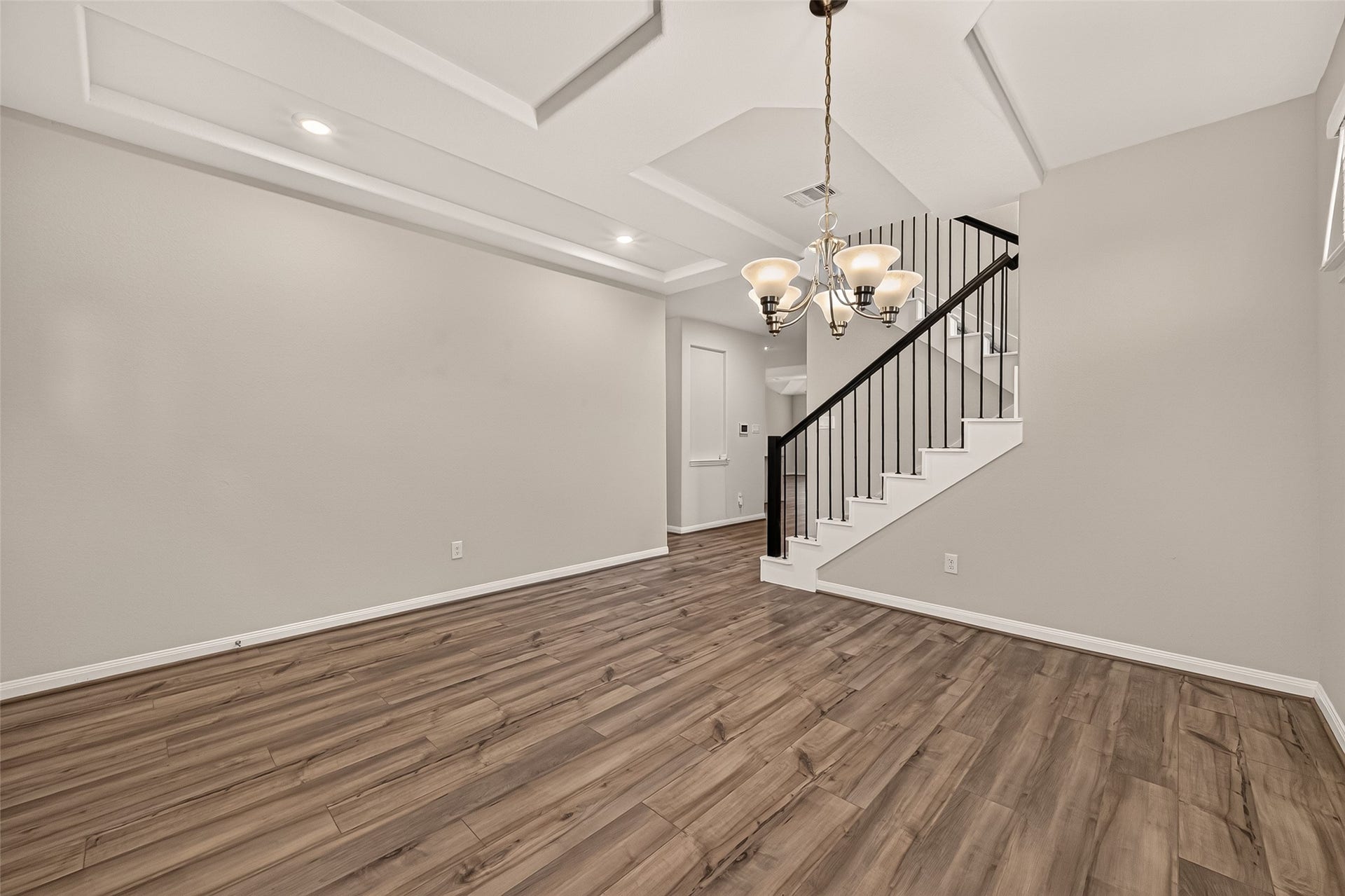 Elegant dining area features a sleek staircase with modern railings, accented by a coffered ceiling with recessed lighting.
