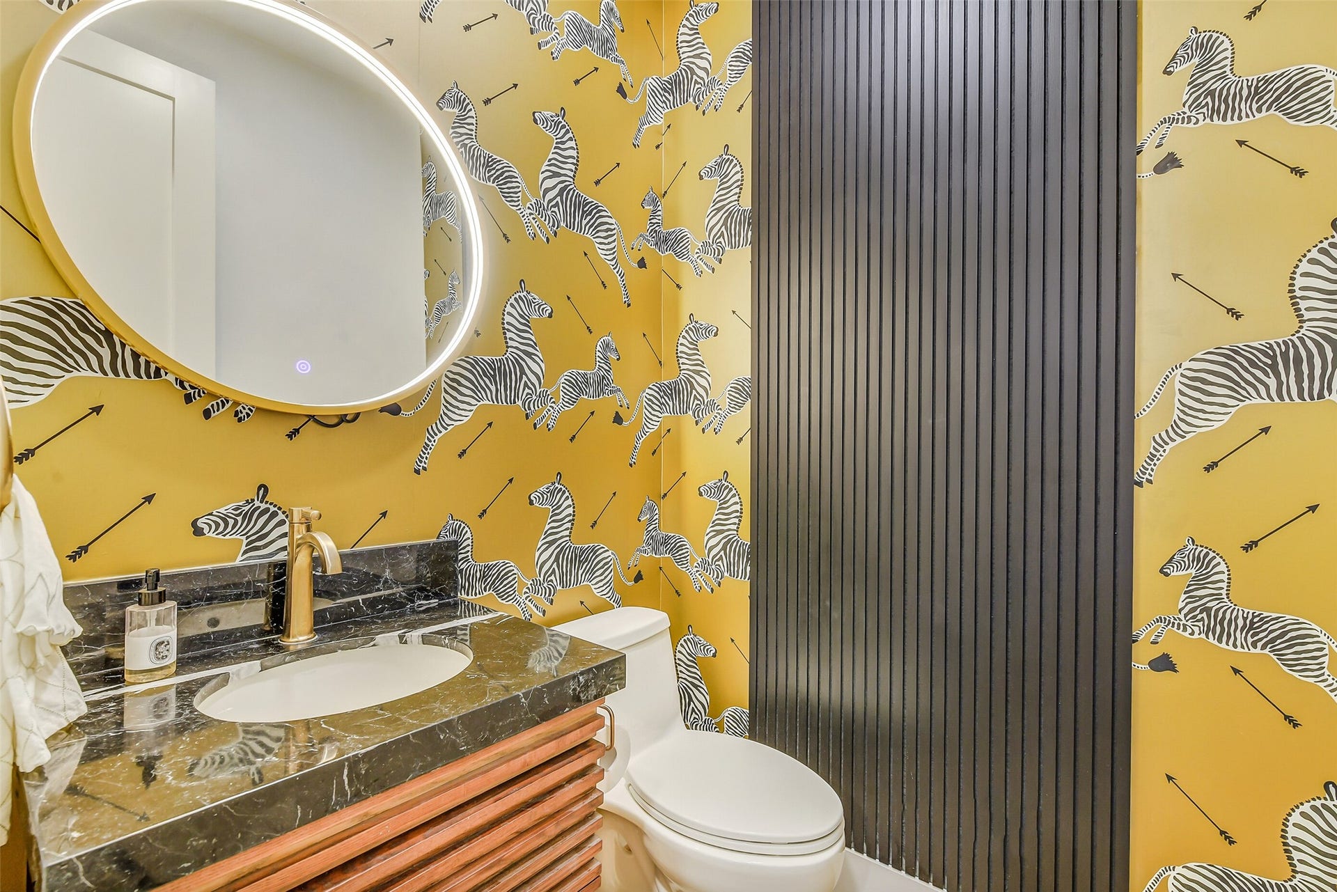 9411 Millbury Drive, Houston, TX 77096 Vibrant, hand-painted-style wallpaper in warm golden hues makes a statement in this powder bath, paired with a sleek floating vanity, oval mirror, and warm brass fixtures for a stylish finish.